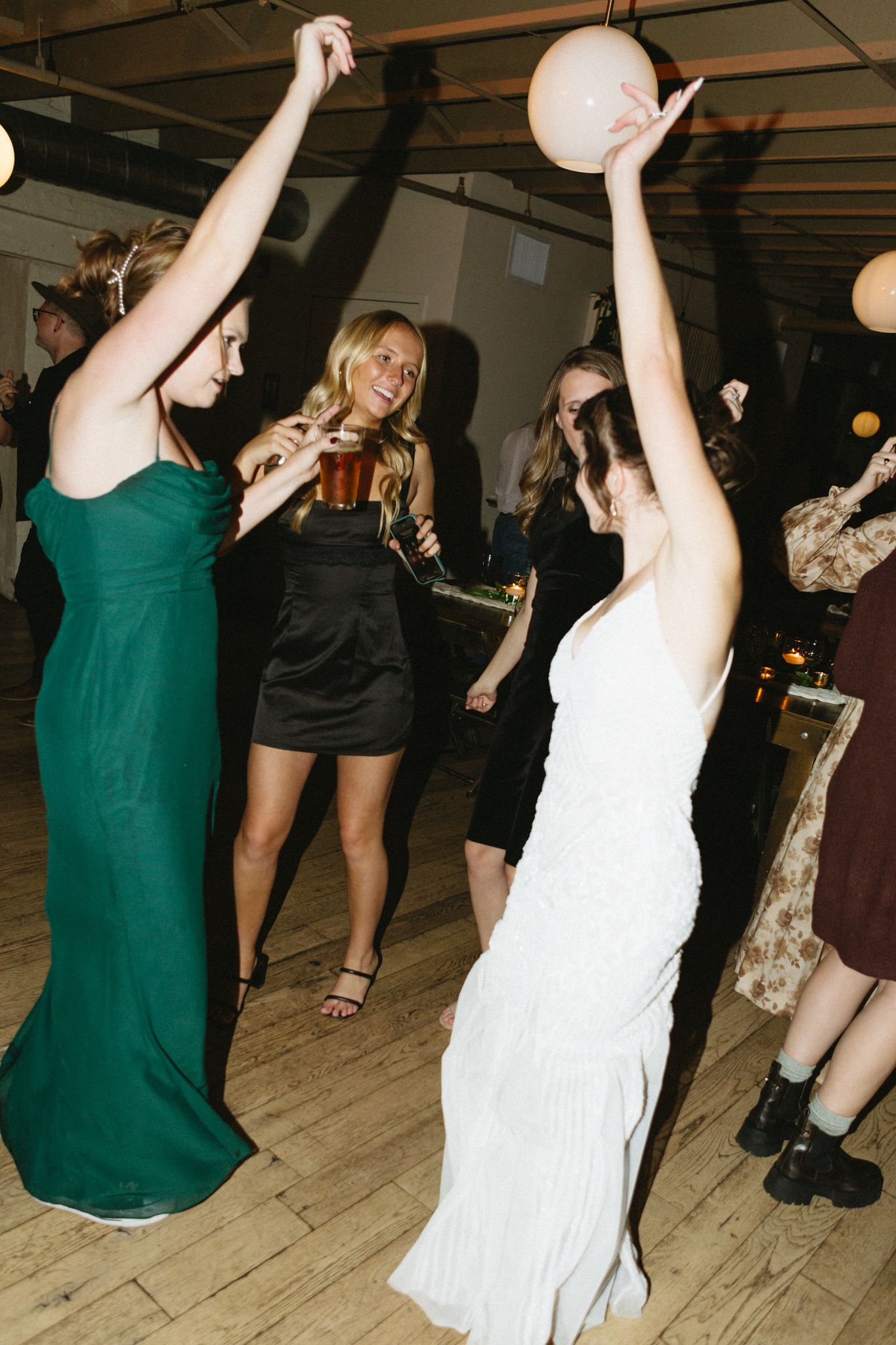 Guests dancing on a wooden floor with raised arms during a celebration.