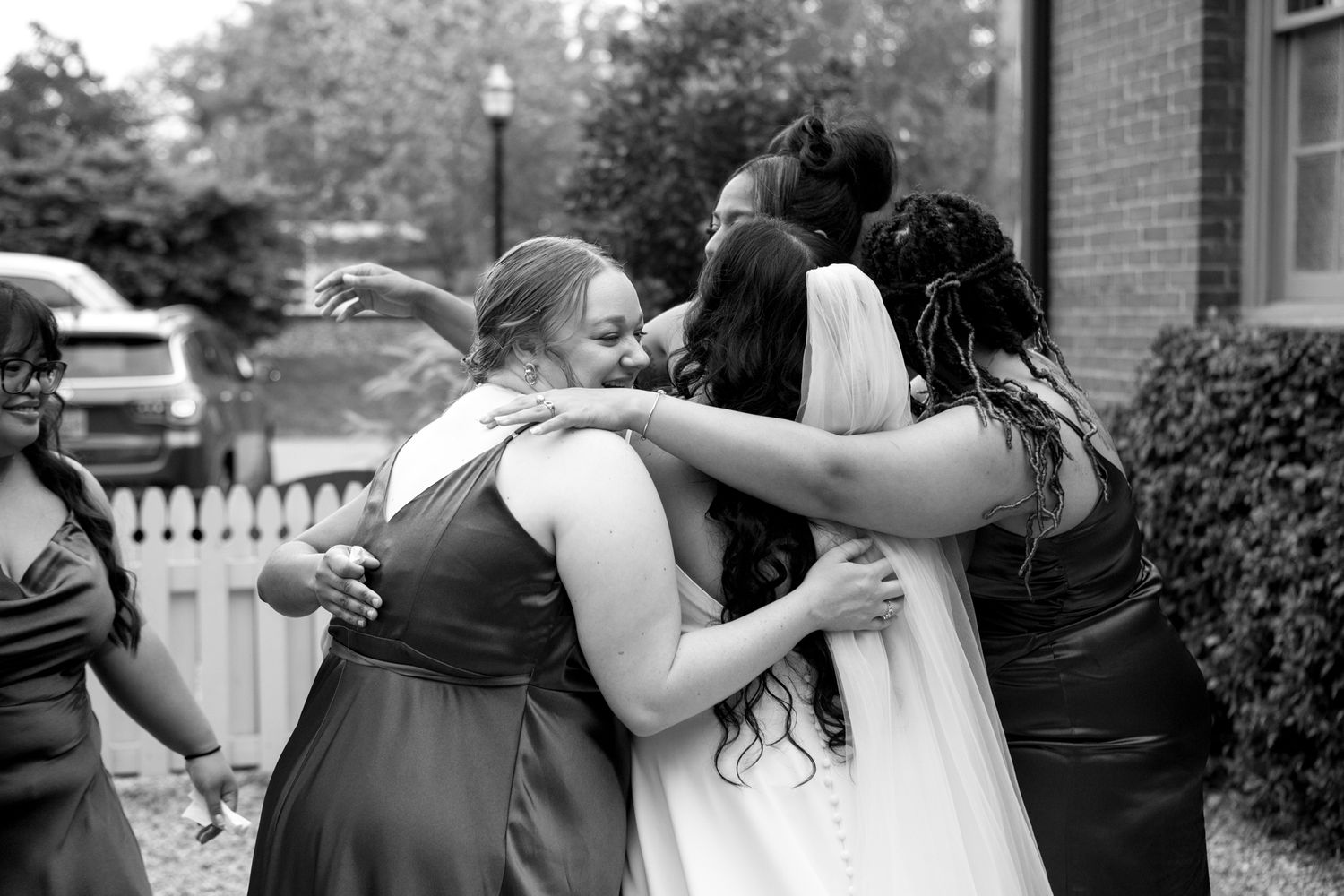 Black and white photo of wedding party members embracing in an emotional group hug outdoors.