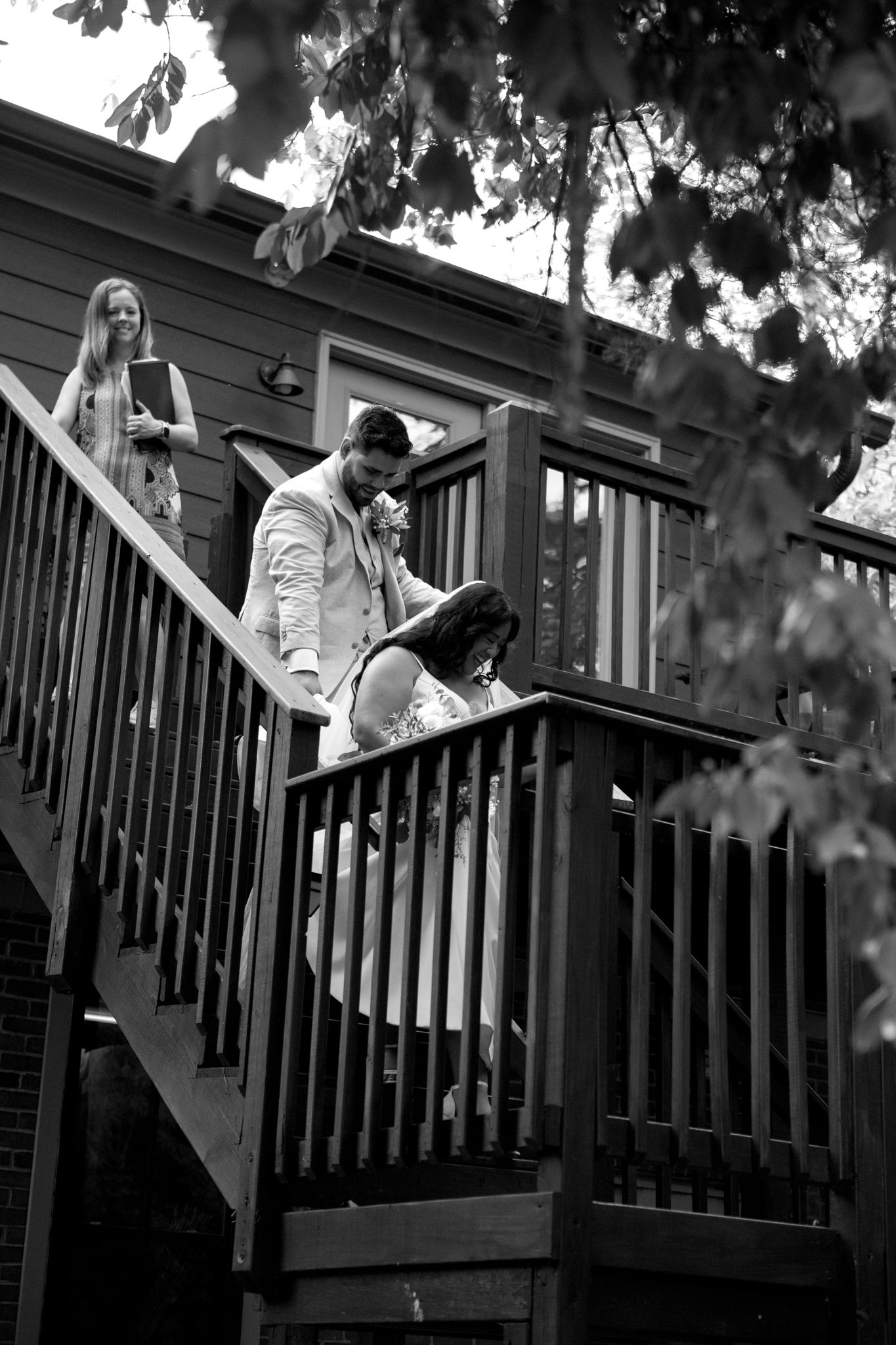 A group of people descend an outdoor wooden staircase in black and white photograph framed by tree branches.