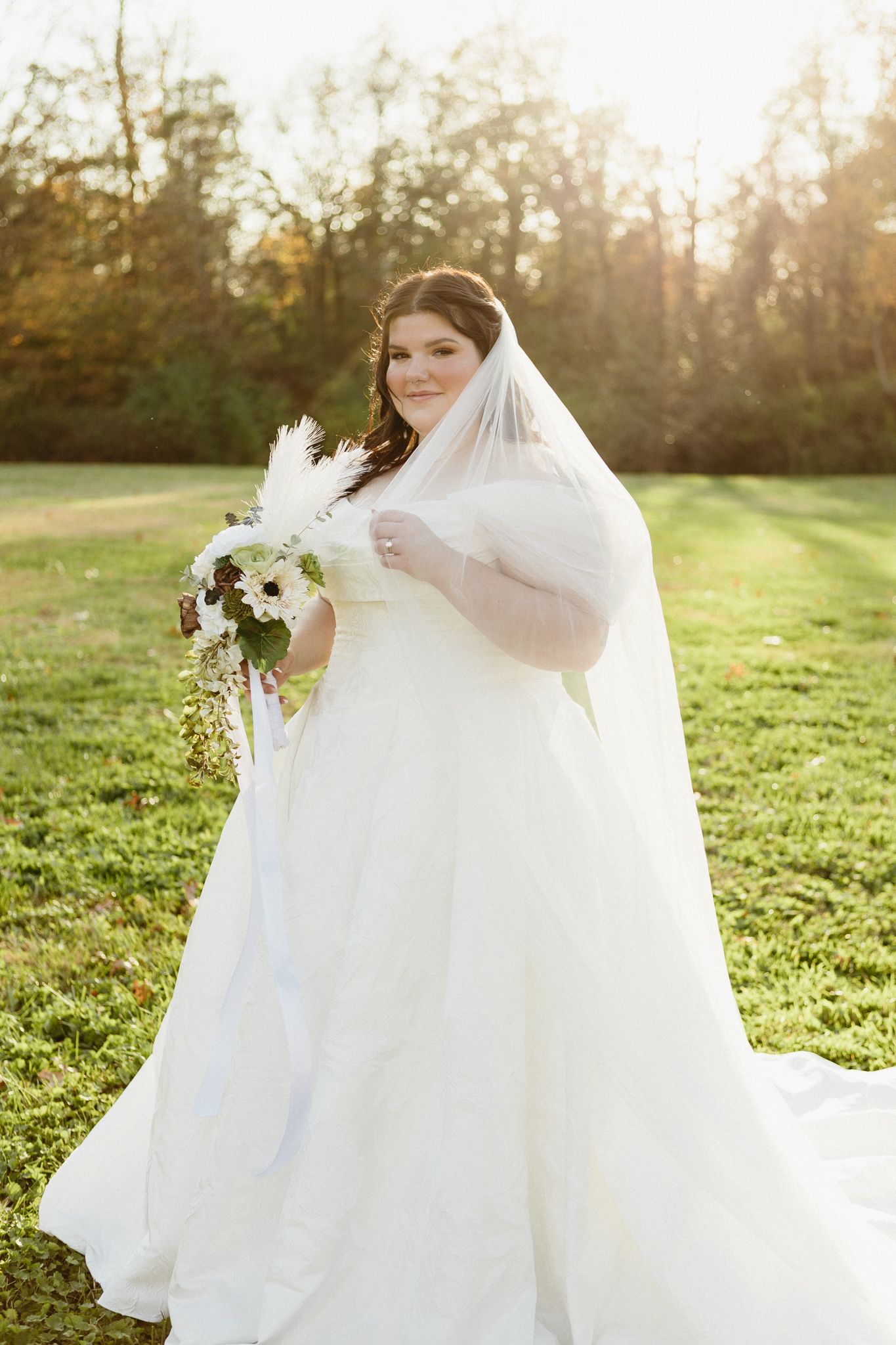 A white wedding gown with flowing train captured in golden hour lighting on a grassy hillside.