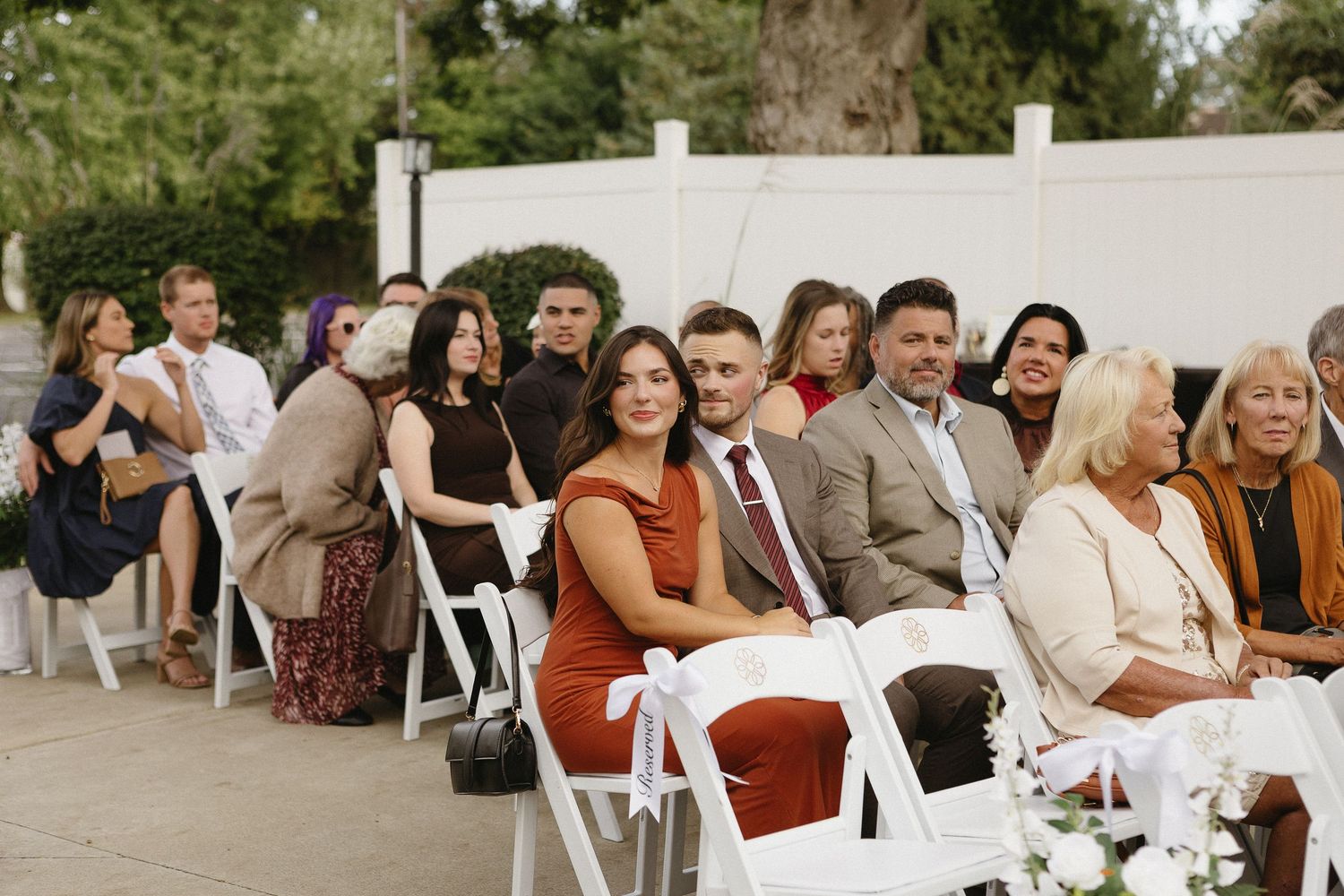 Wedding guests seated in white chairs at an outdoor ceremony.