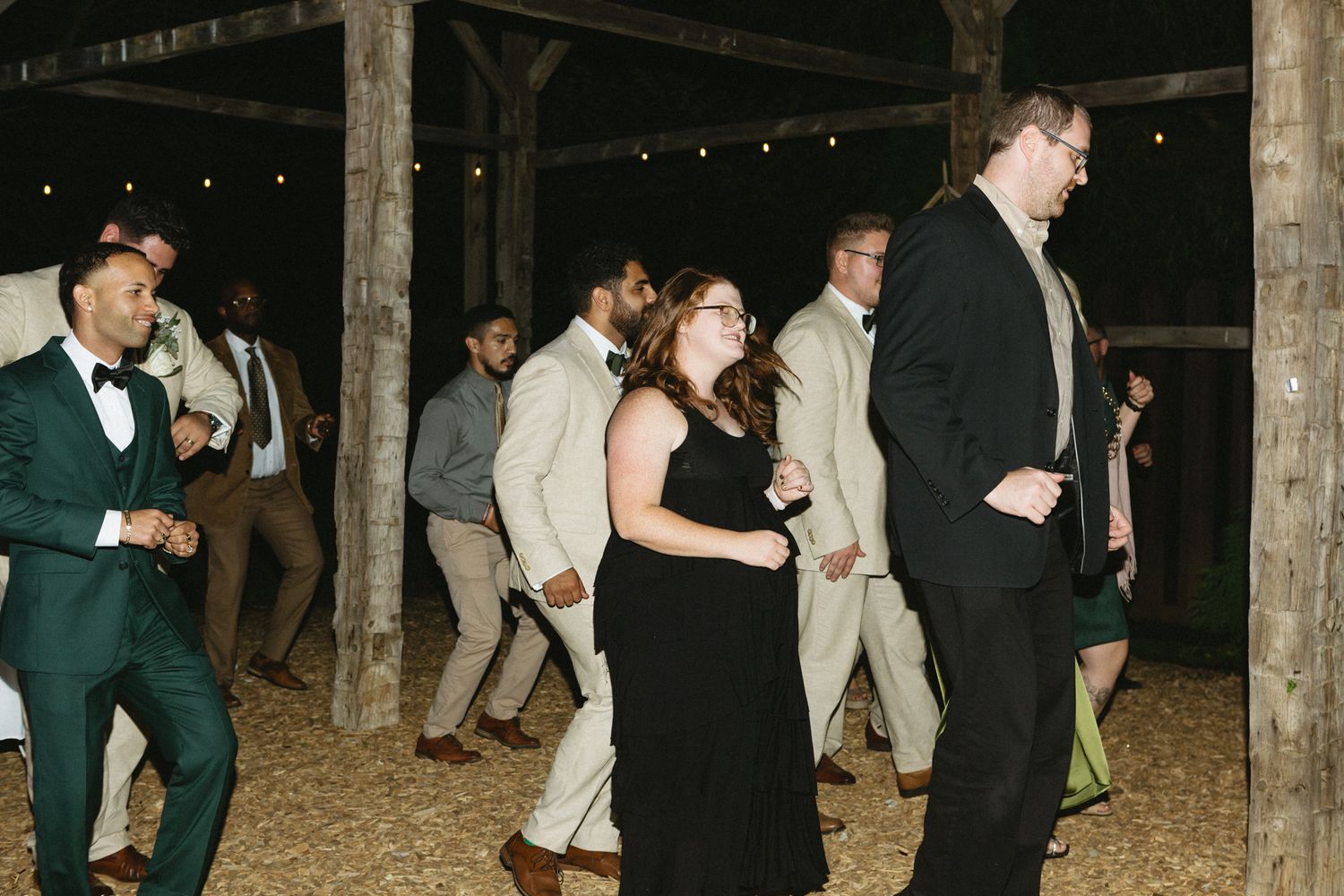 A group of people dancing and celebrating at night under string lights at an outdoor party.