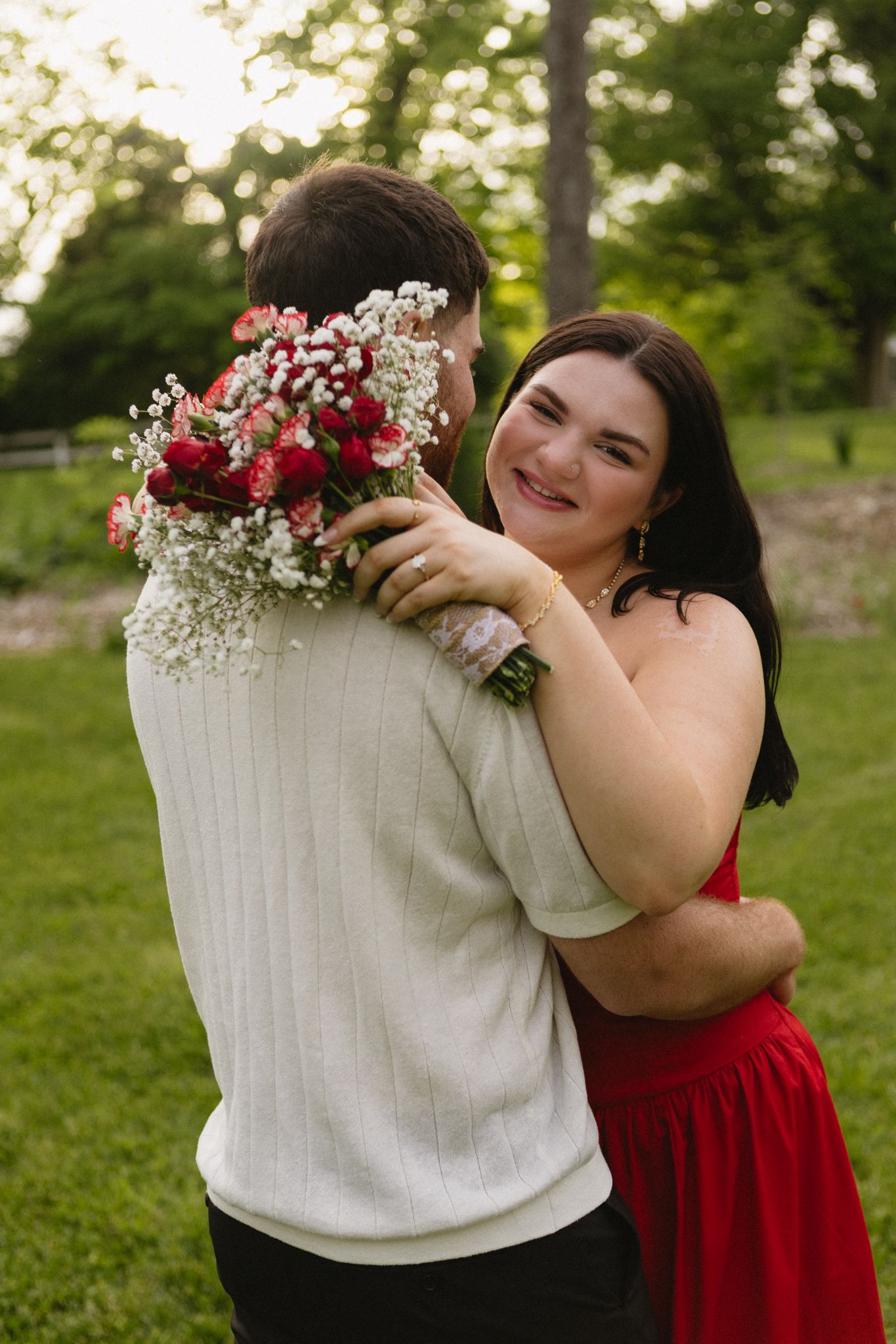 A romantic embrace features red and white attire with a delicate bouquet of baby's breath and roses against a garden backdrop.