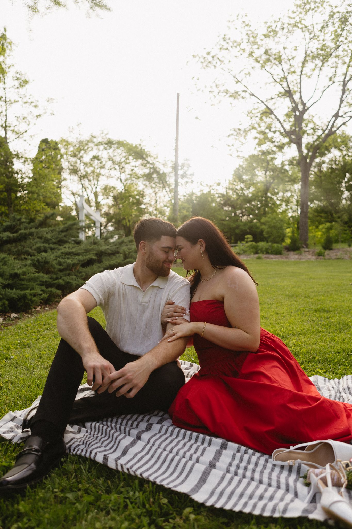 A couple shares an intimate moment on a striped blanket during a summer outdoor picnic in a park.