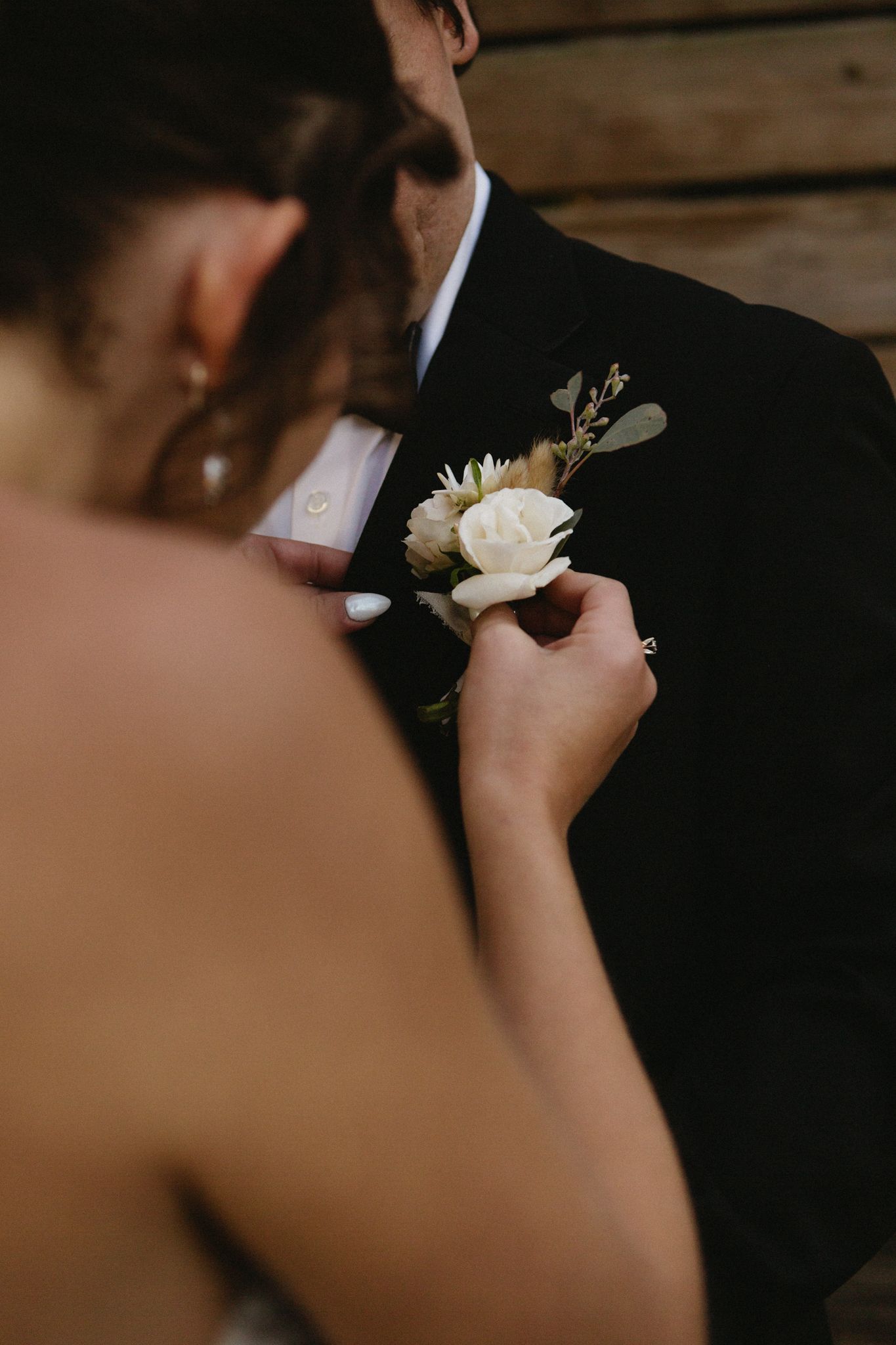 Close-up of hands pinning a white rose boutonniere to a black suit jacket.