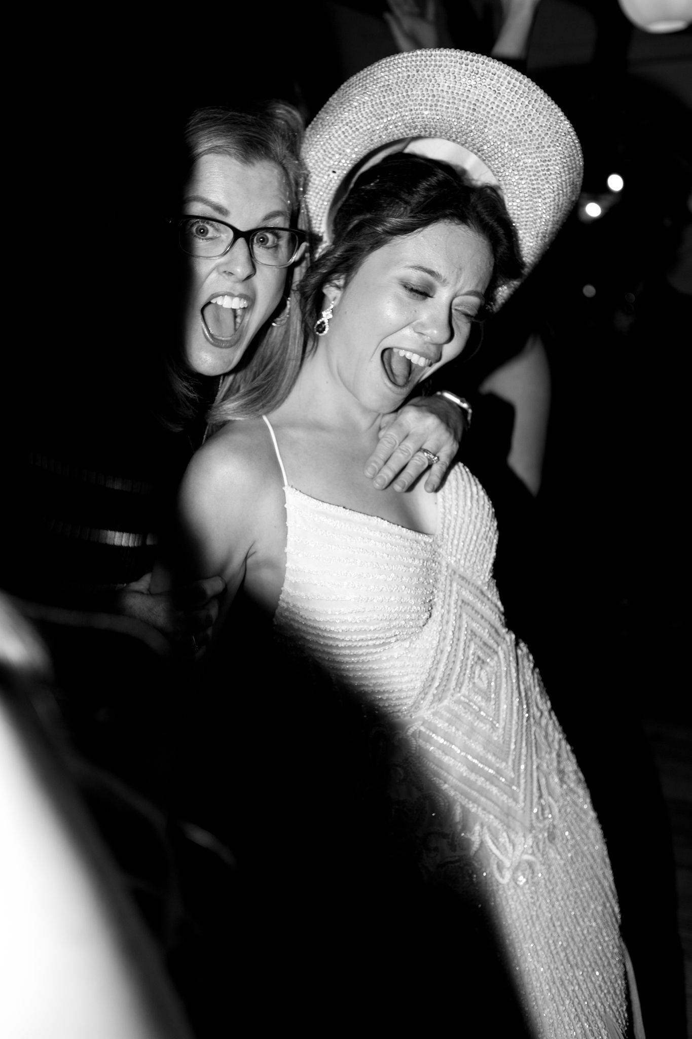 A couple shares a joyful candid moment at a celebration, with the bride wearing a white dress and sparkly headpiece.