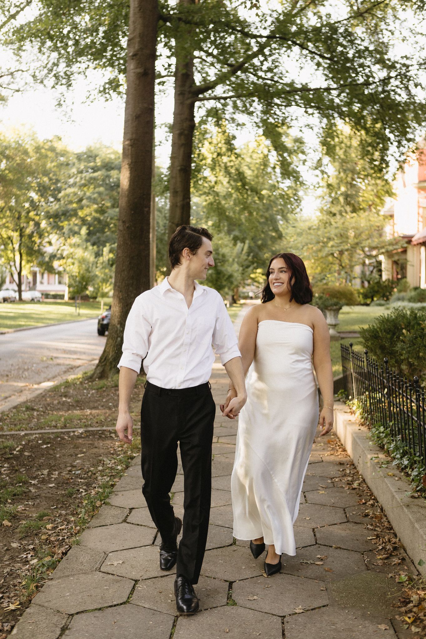 A couple walking together on a stone pathway surrounded by trees on a sunny autumn day.