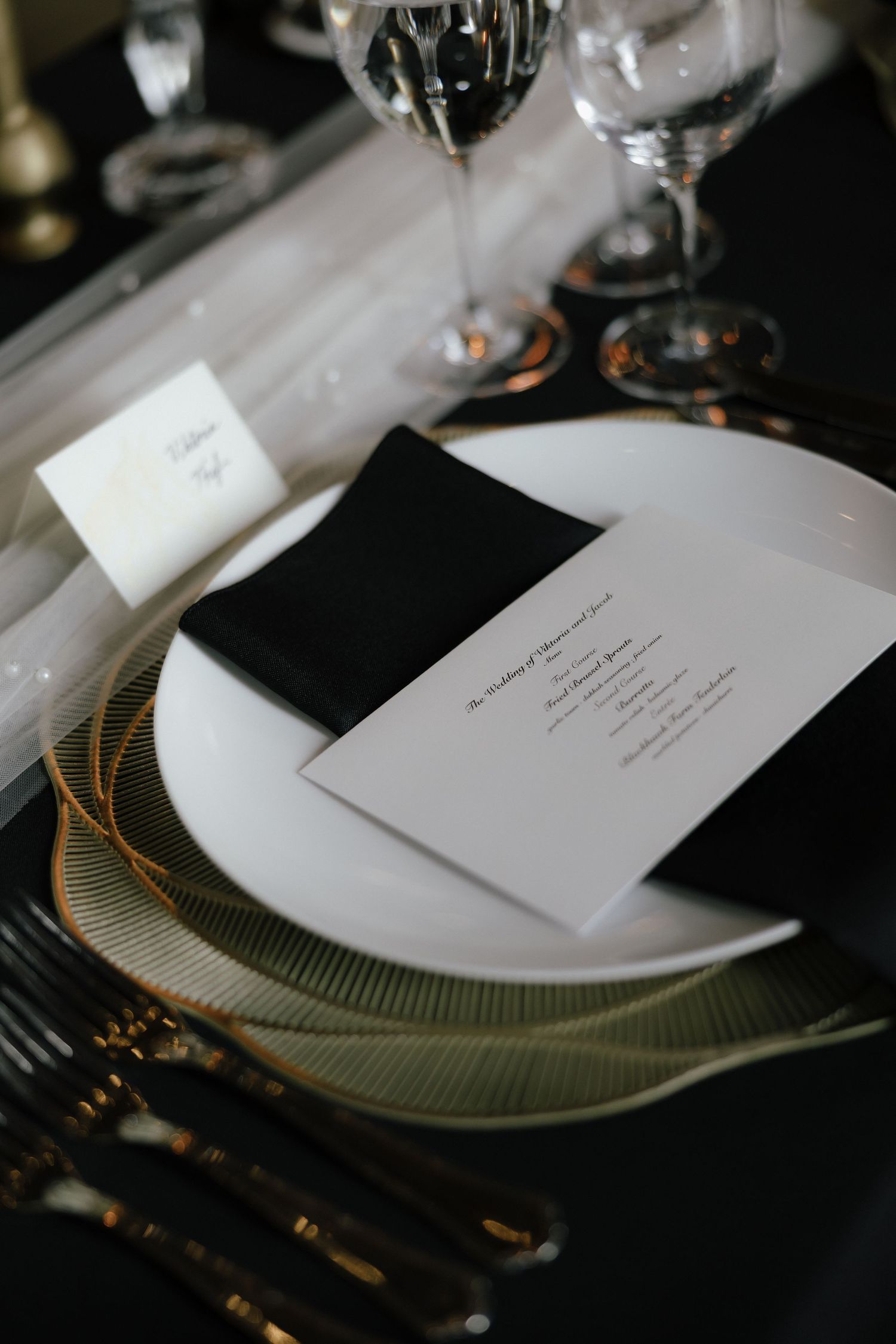 Elegant wedding place setting with white plate, black napkin, menu card, and crystal glassware.