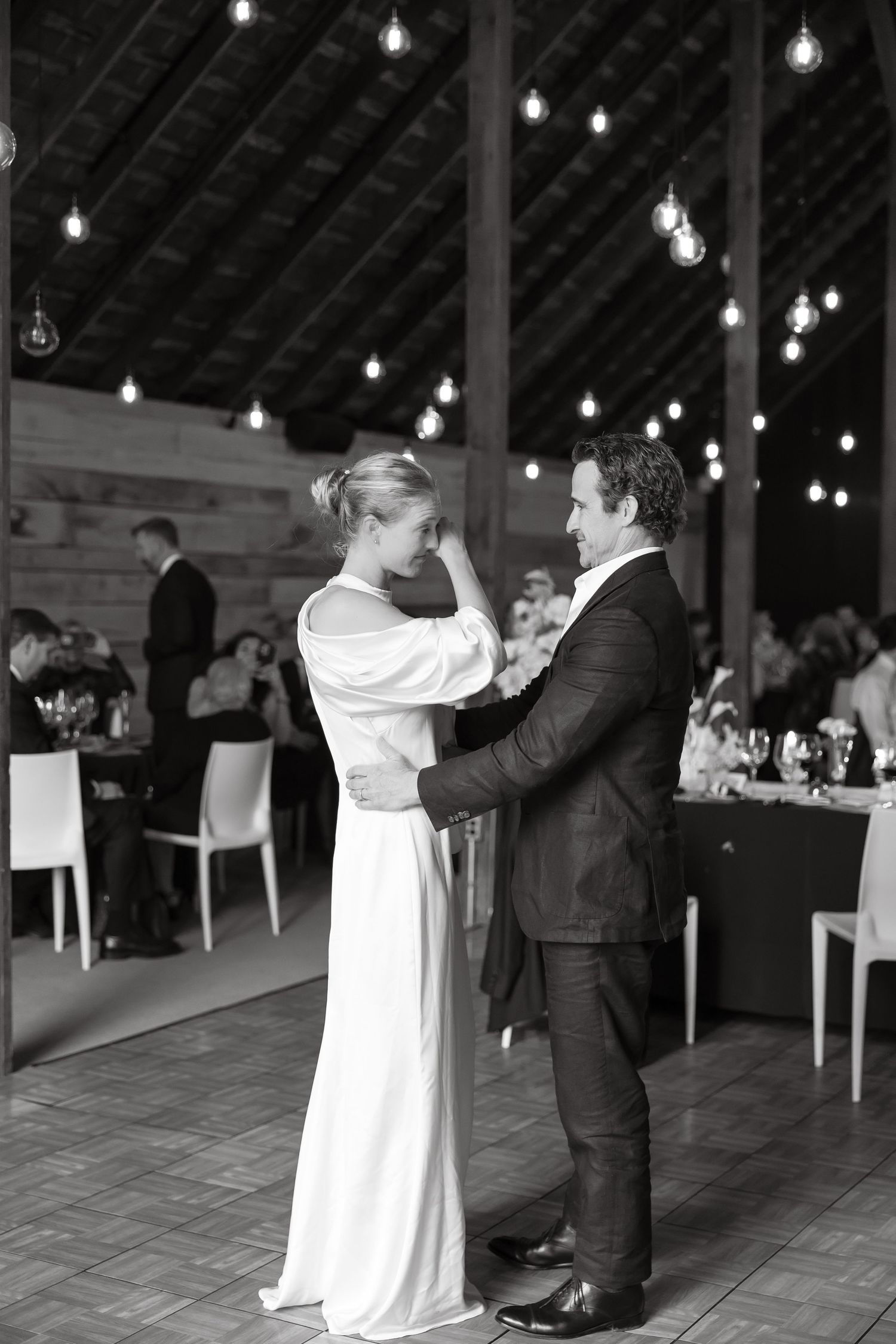 Black and white photo of bride and groom sharing first dance in elegant barn reception venue.