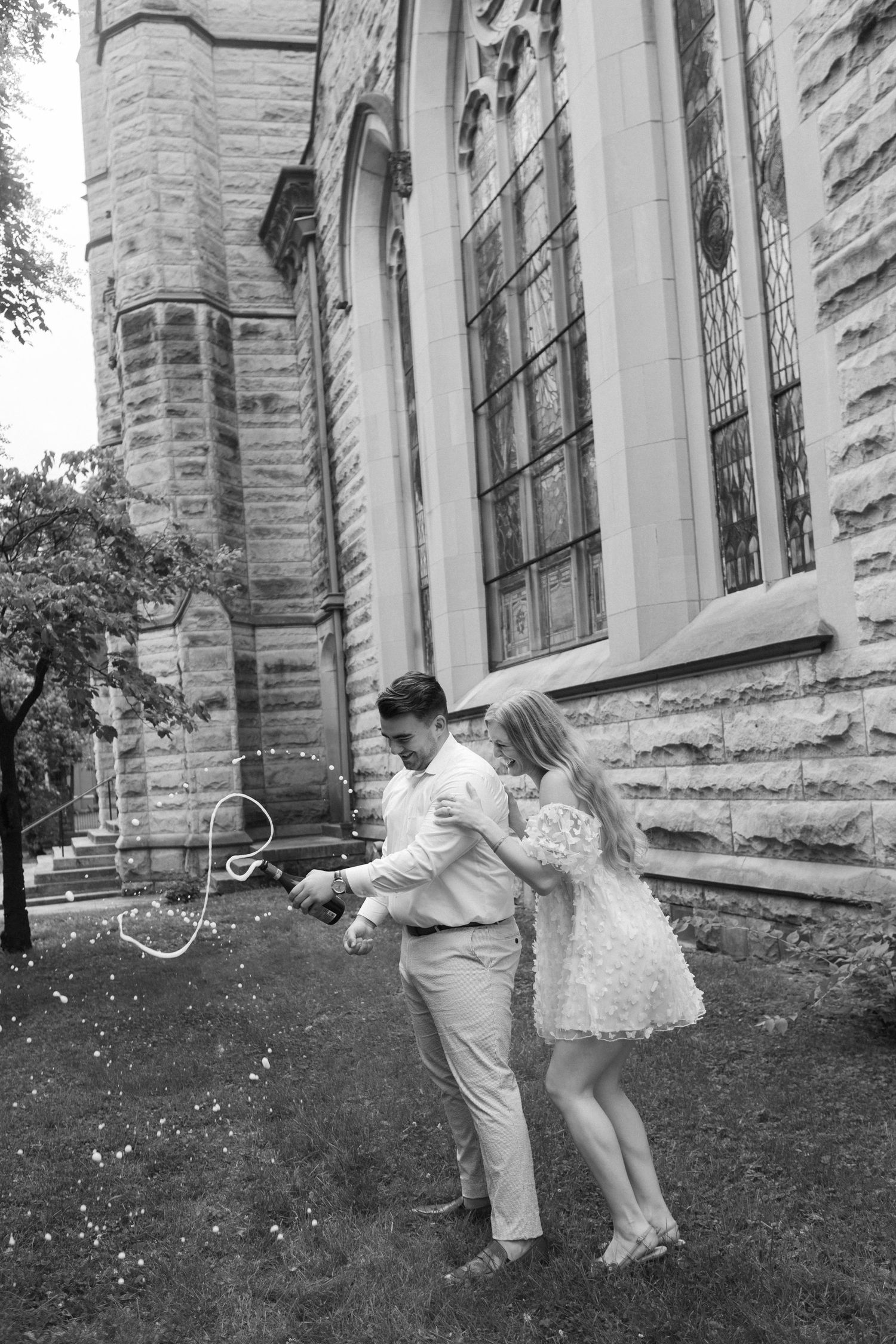 Black and white photo of a couple dancing outside a historic stone church on their wedding day.