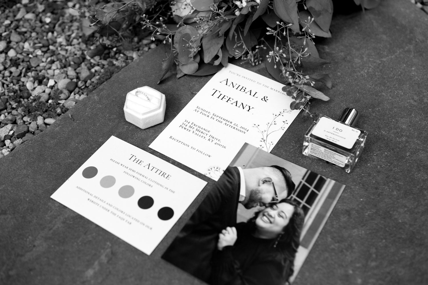 Black and white photograph of wedding stationery including menus, cards, and other paper materials arranged on a dark surface.