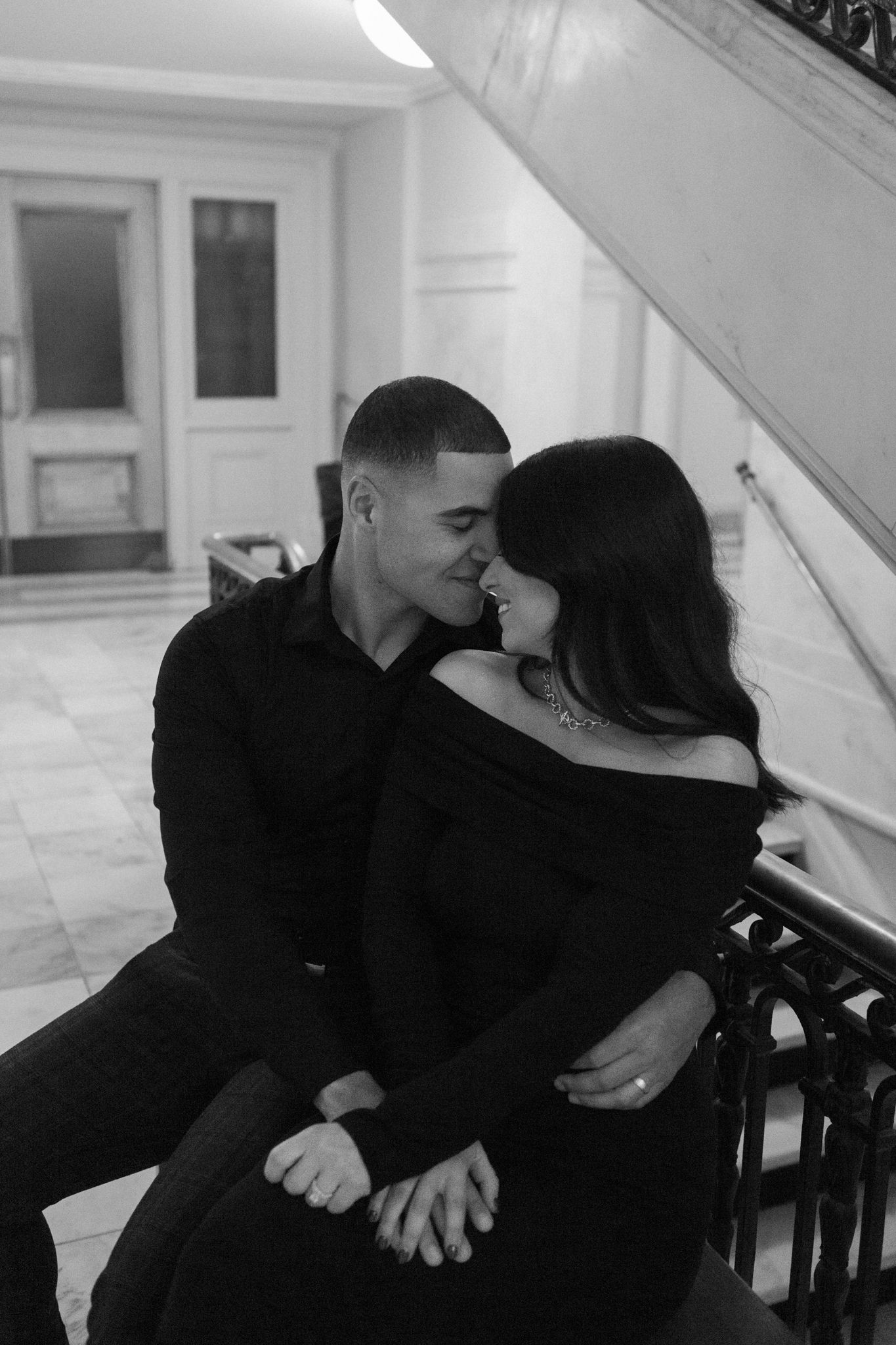Intimate couple in black clothing share a tender moment while sitting on elegant marble stairs.