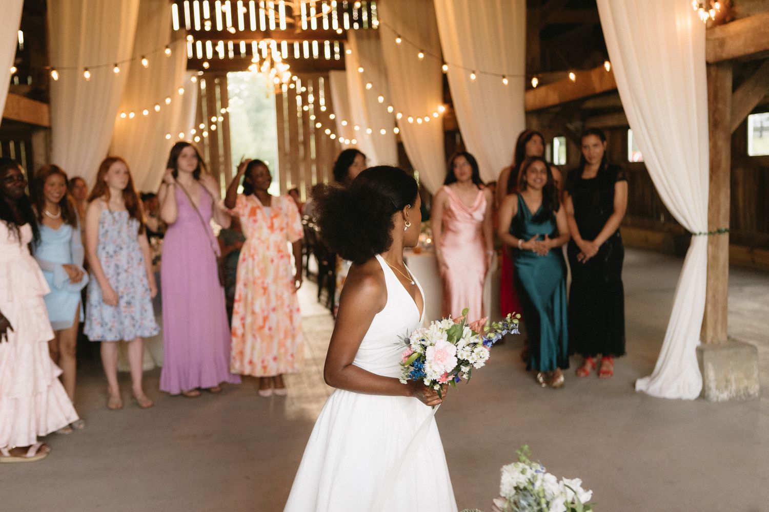 Wedding reception celebration in a rustic barn decorated with string lights and white drapes.