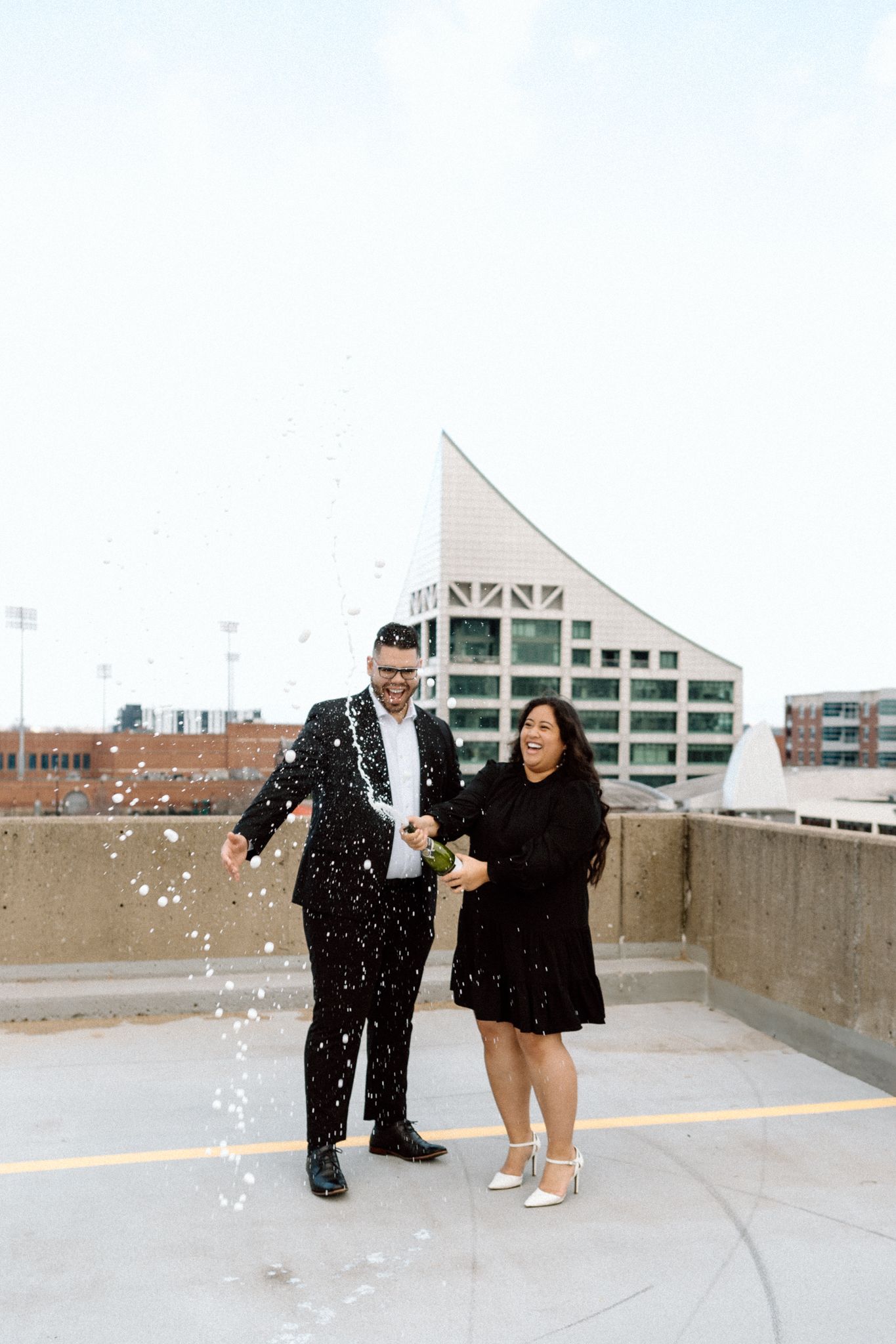 Engaged couple celebrating with a bottle of Chandon, sharing a joyful moment and laughter in downtown Louisville