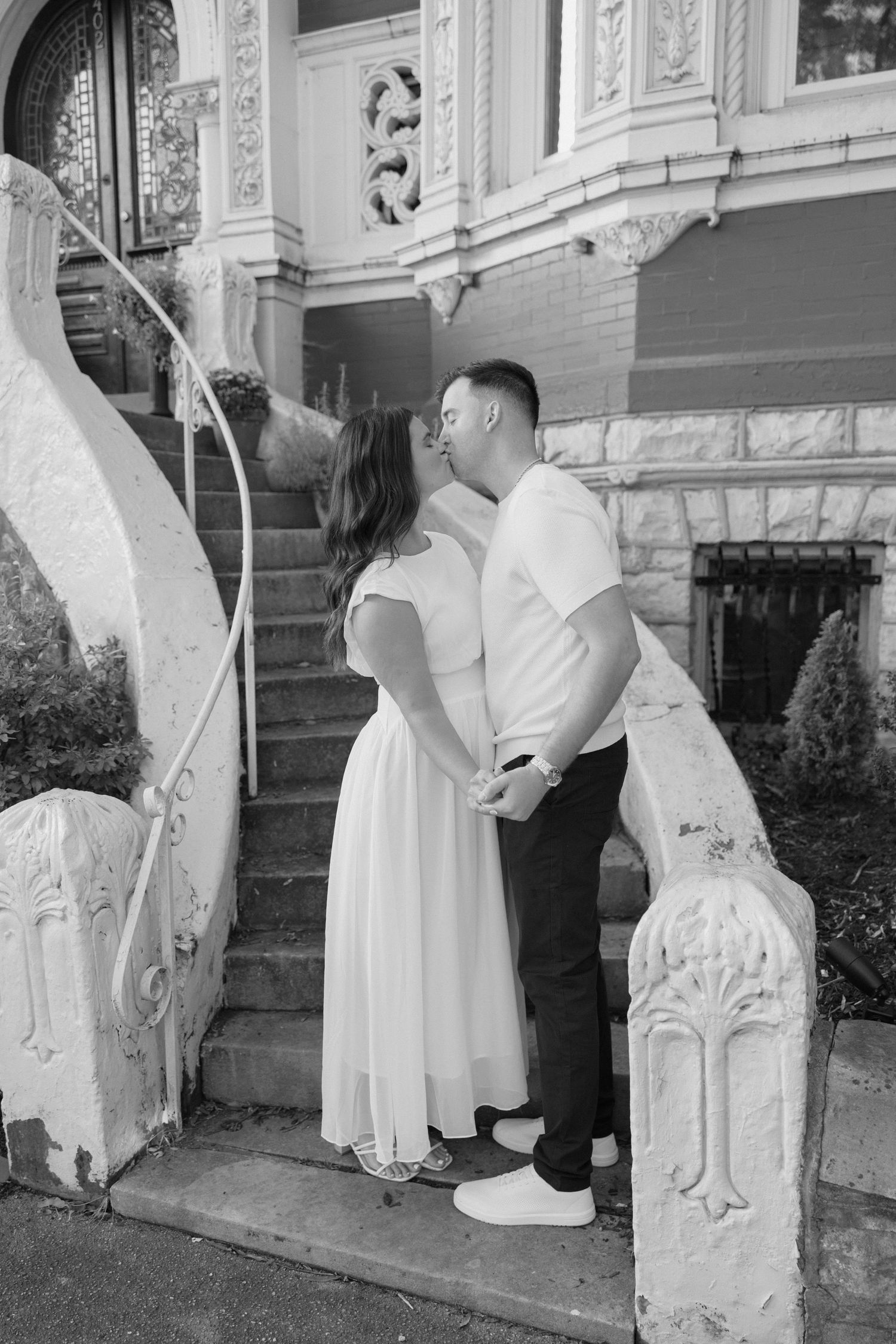 Black and white photo of a couple kissing on ornate stone steps of a historic building.
