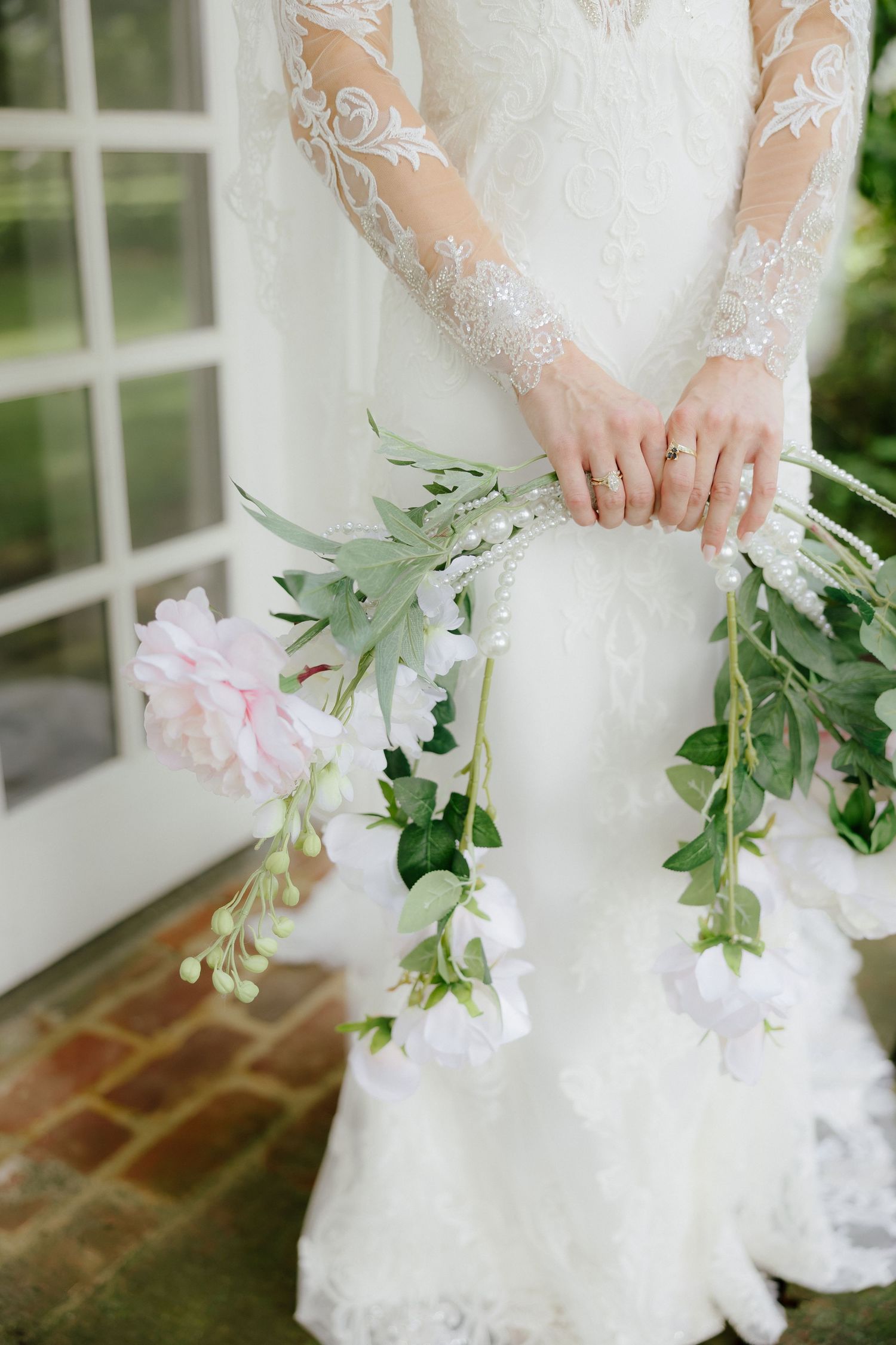 Bride in lace long-sleeve wedding dress holding cascading pink and white floral bouquet with greenery.