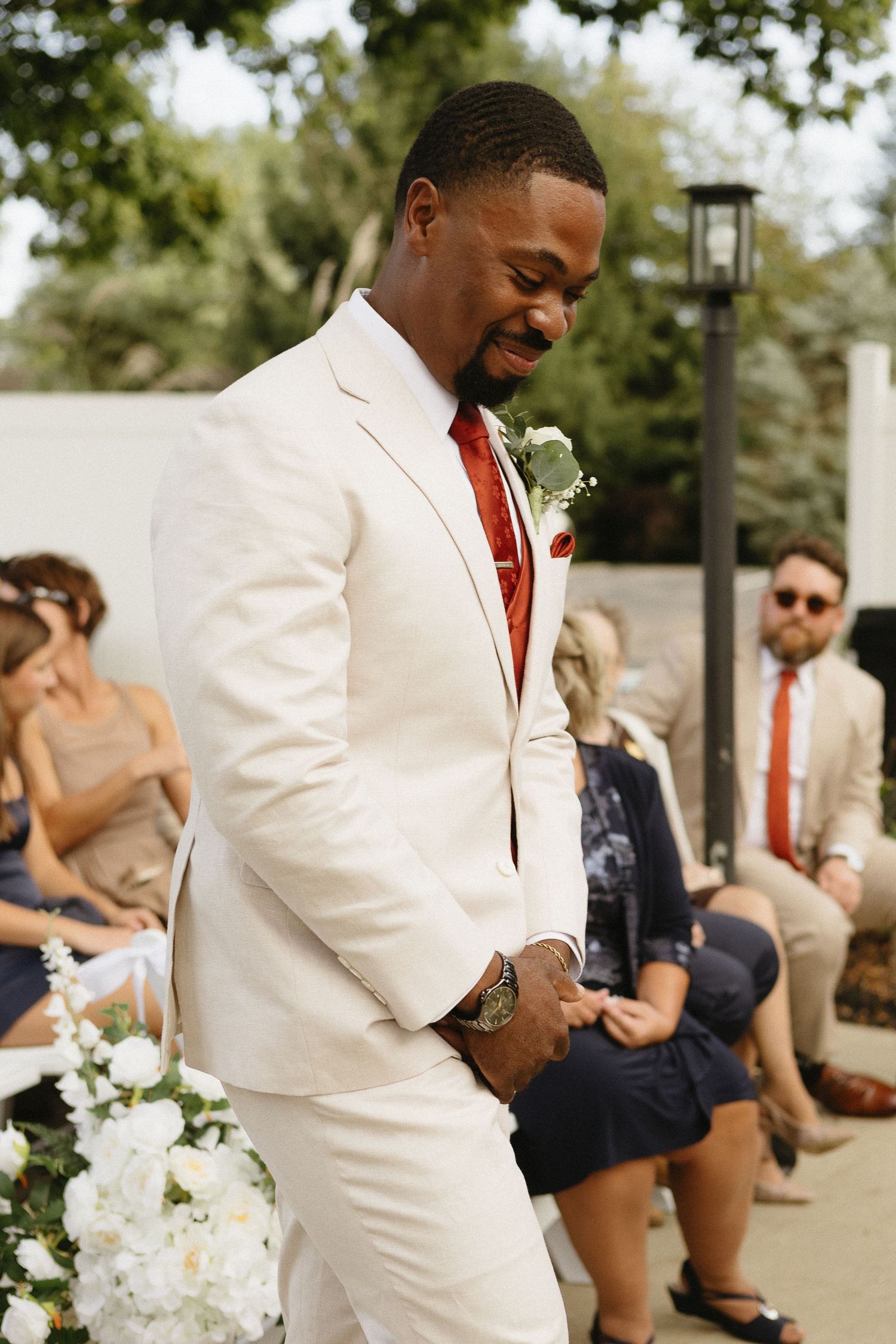 Wedding party members in cream suits with burgundy ties walking outdoors.