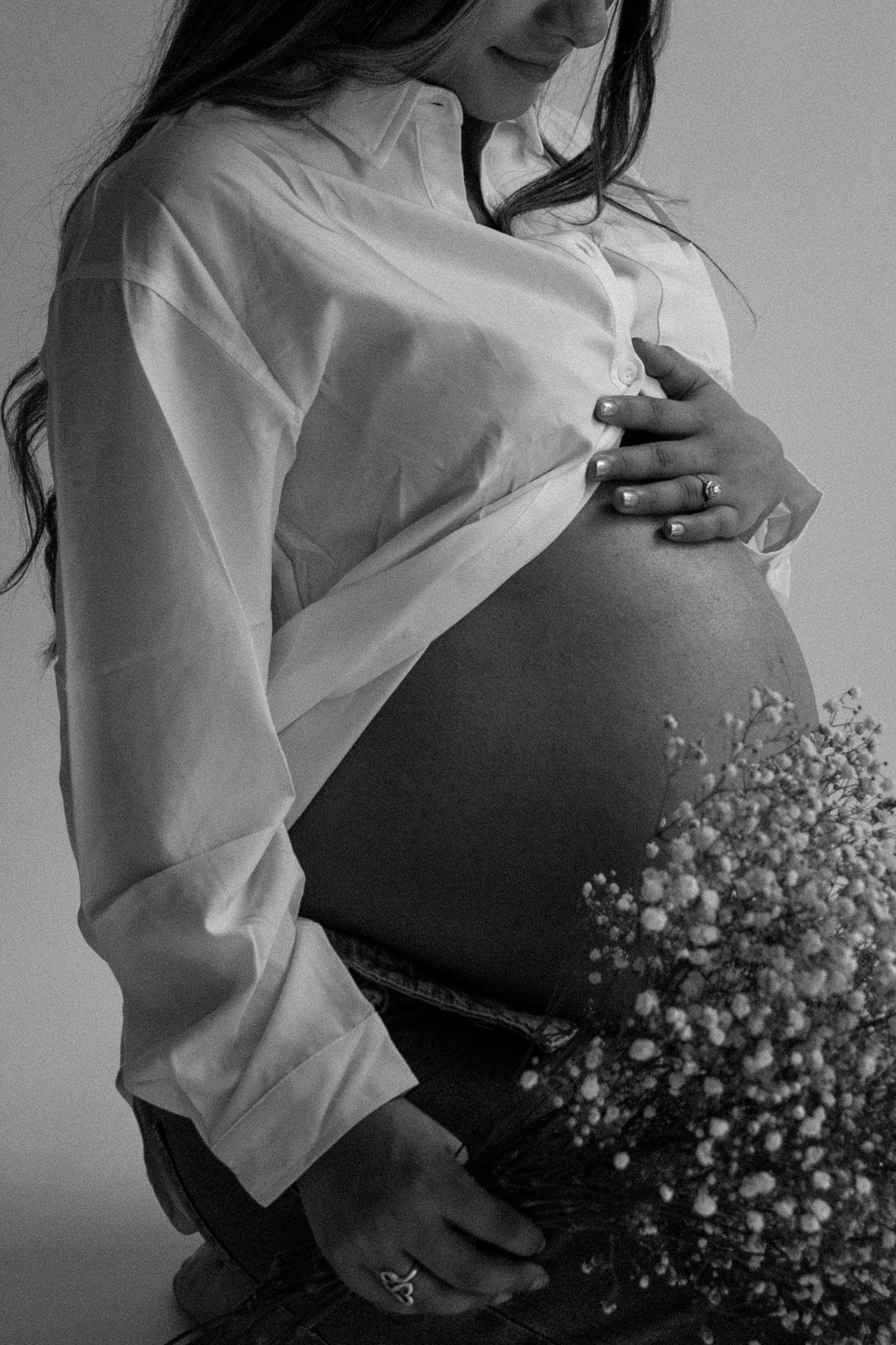 Close-up of a pregnant woman's hands gently cradling her belly, in a serene and intimate indoor maternity photoshoot