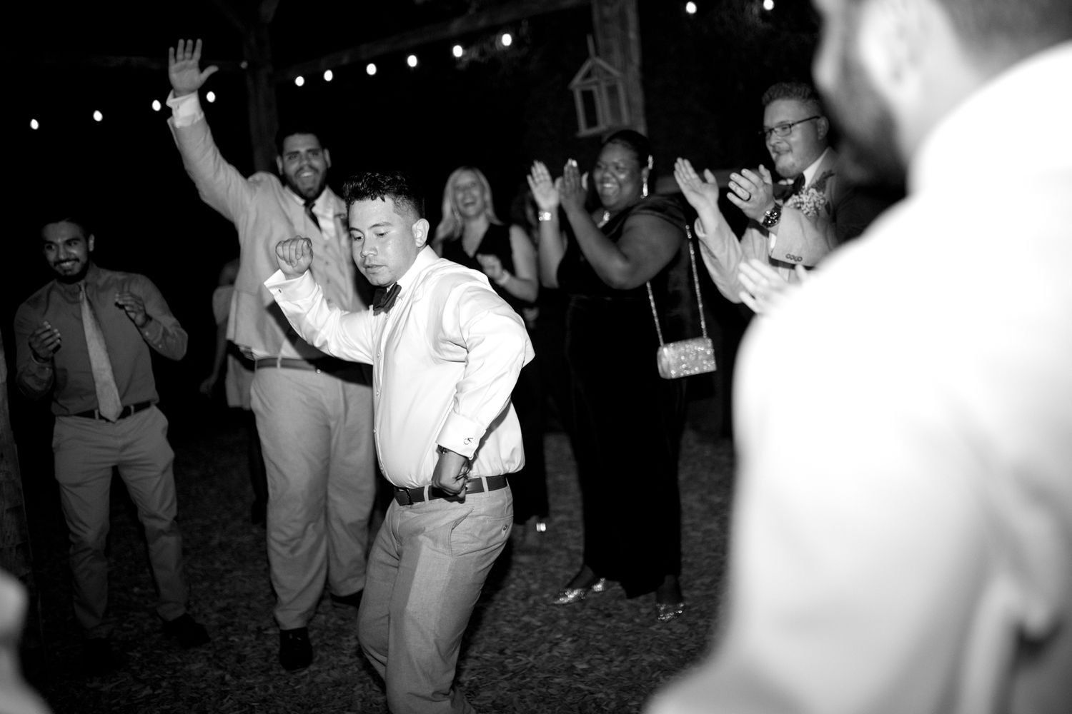 A group of people dancing and celebrating at night under string lights at an outdoor party.