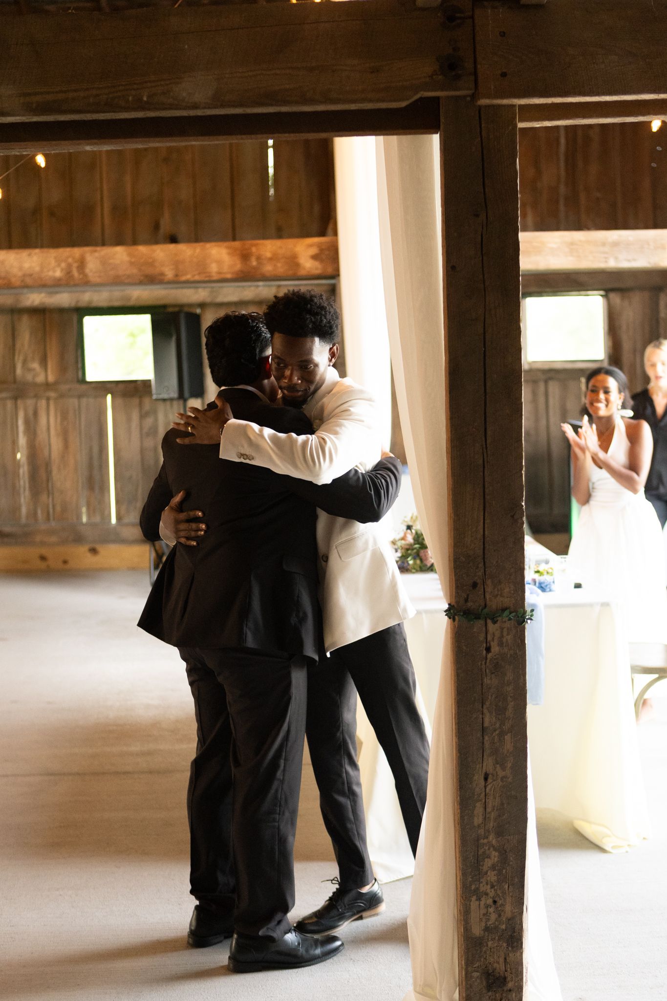 Emotional wedding party members embrace and celebrate in a dimly lit rustic wooden venue.