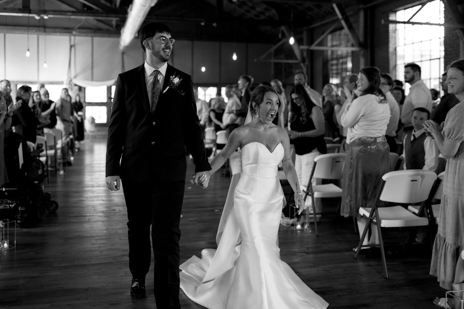 bride and groom walking down the aisle showing new wedding rings and smiling black and white photo