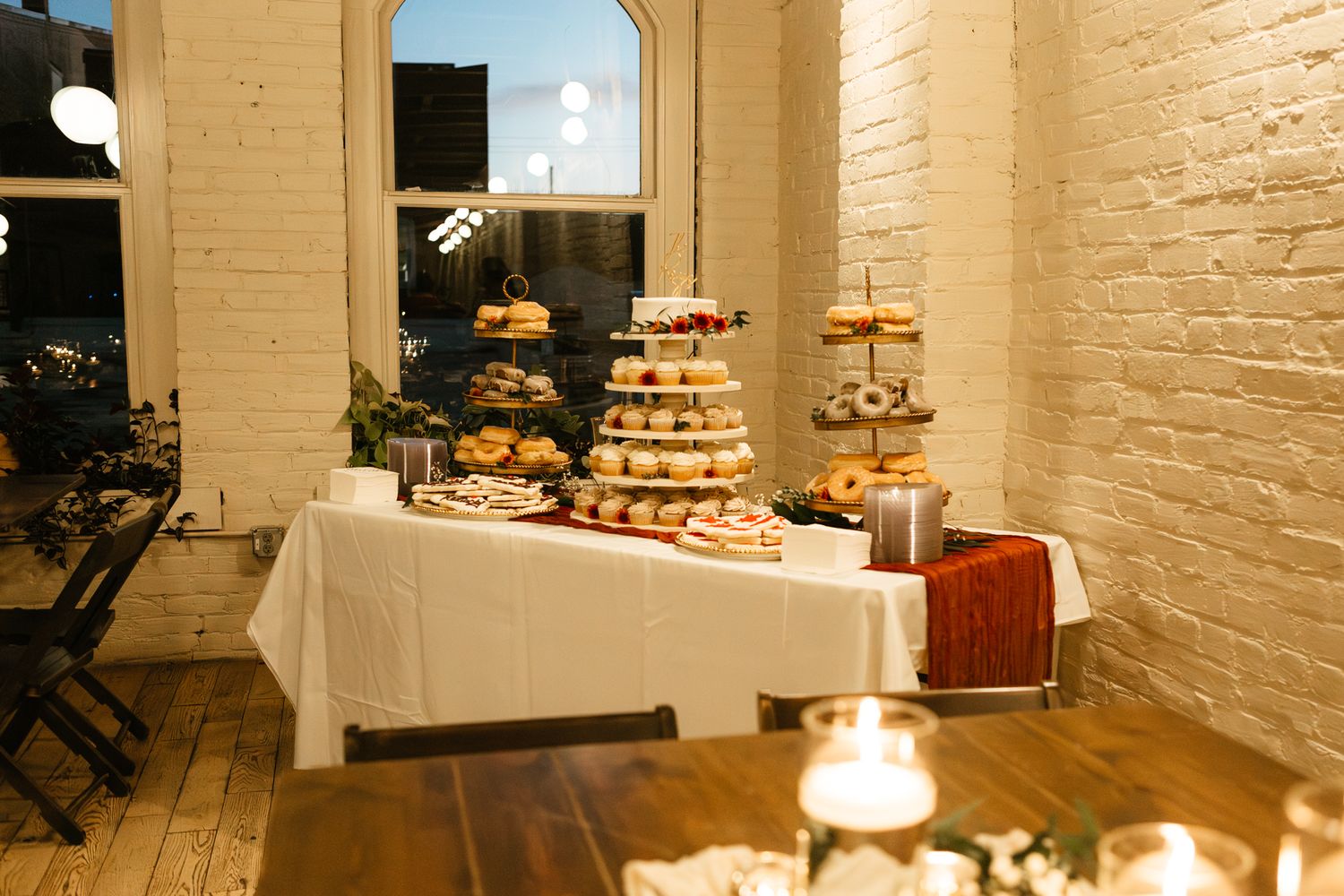 An elegant dessert table with tiered displays of treats against white brick walls.