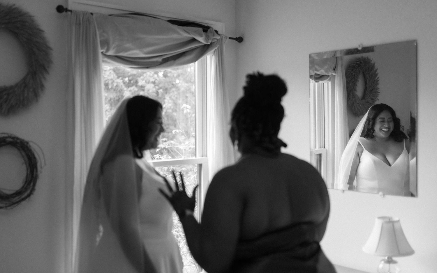 A black and white wedding scene showing a bridal party getting ready in front of window and mirror.