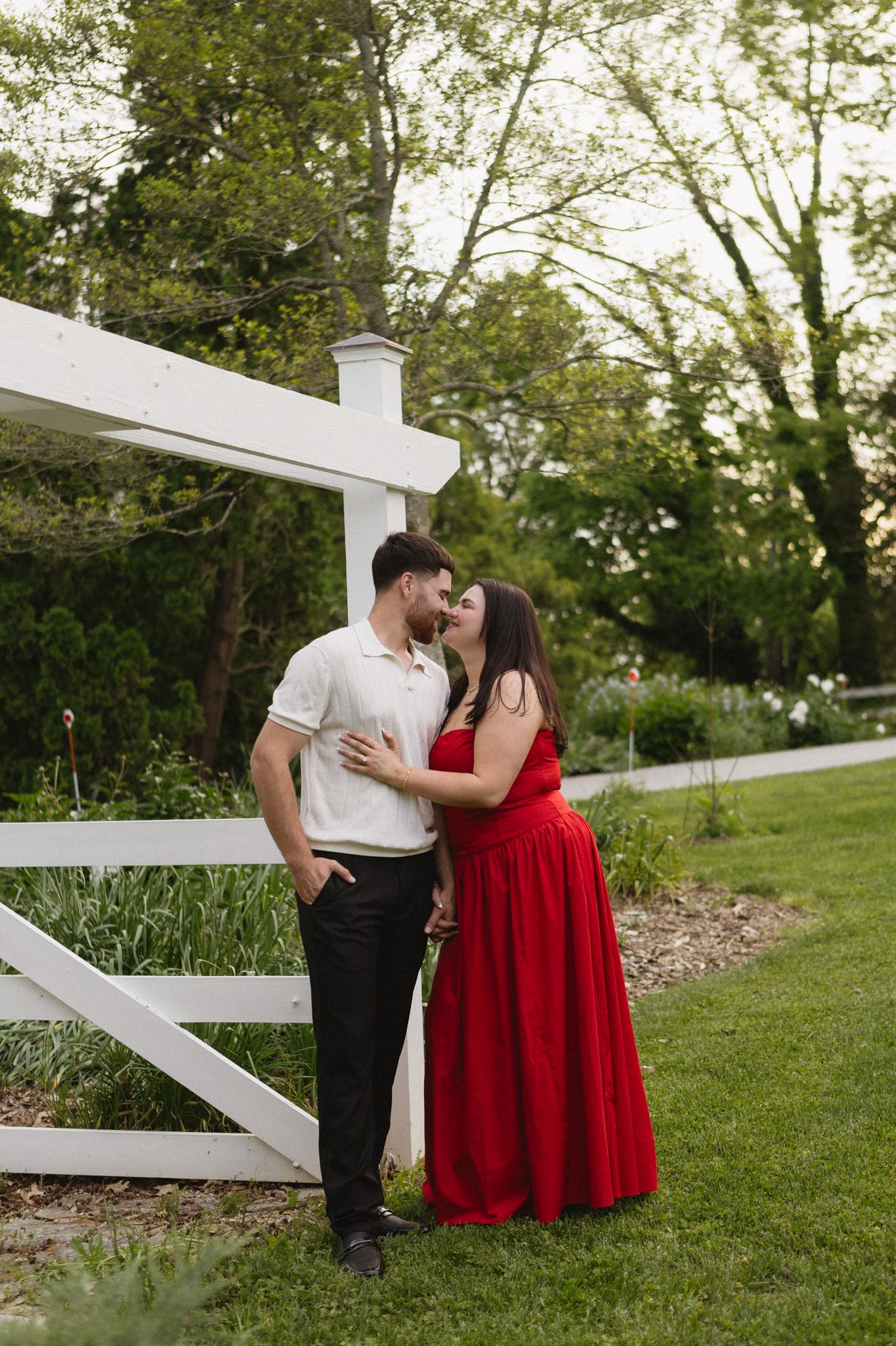 A romantic moment between a couple by a white fence in a garden setting.