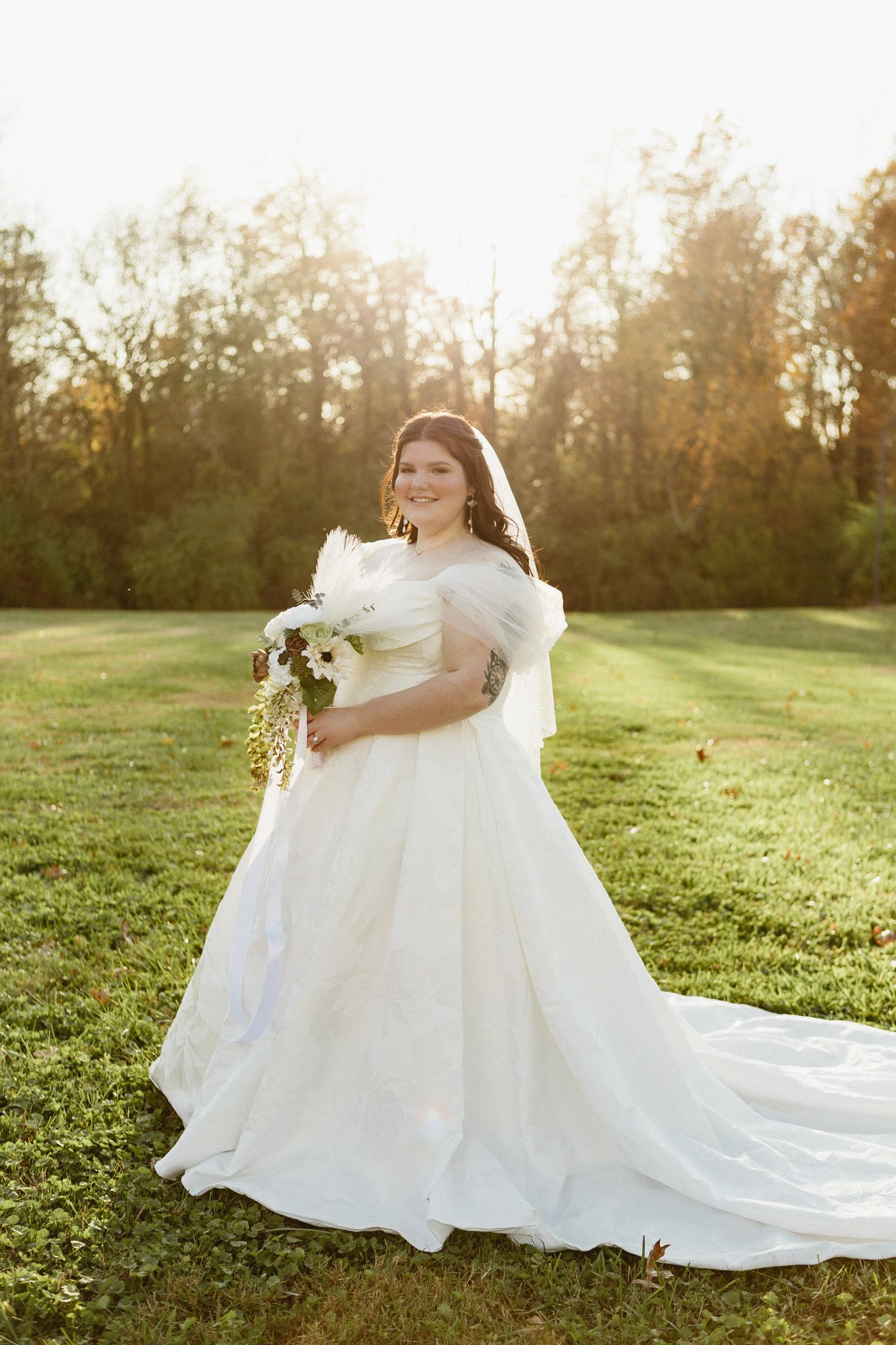 A person in a flowing white wedding gown sits gracefully in a sunlit meadow during golden hour.
