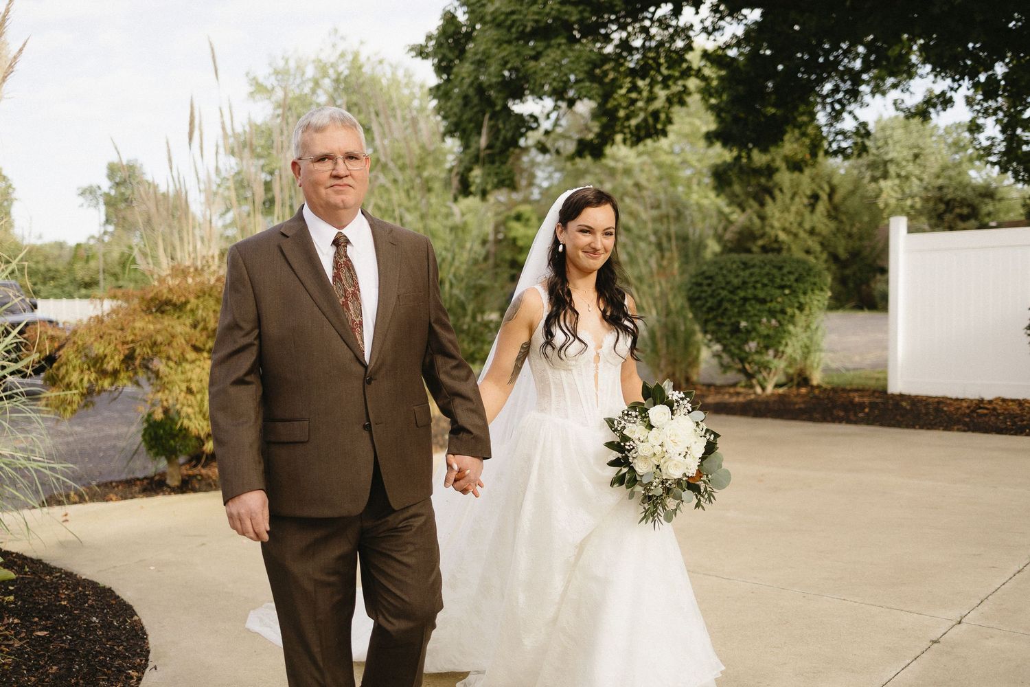 Outdoor wedding portrait with lush greenery and white floral arrangements.