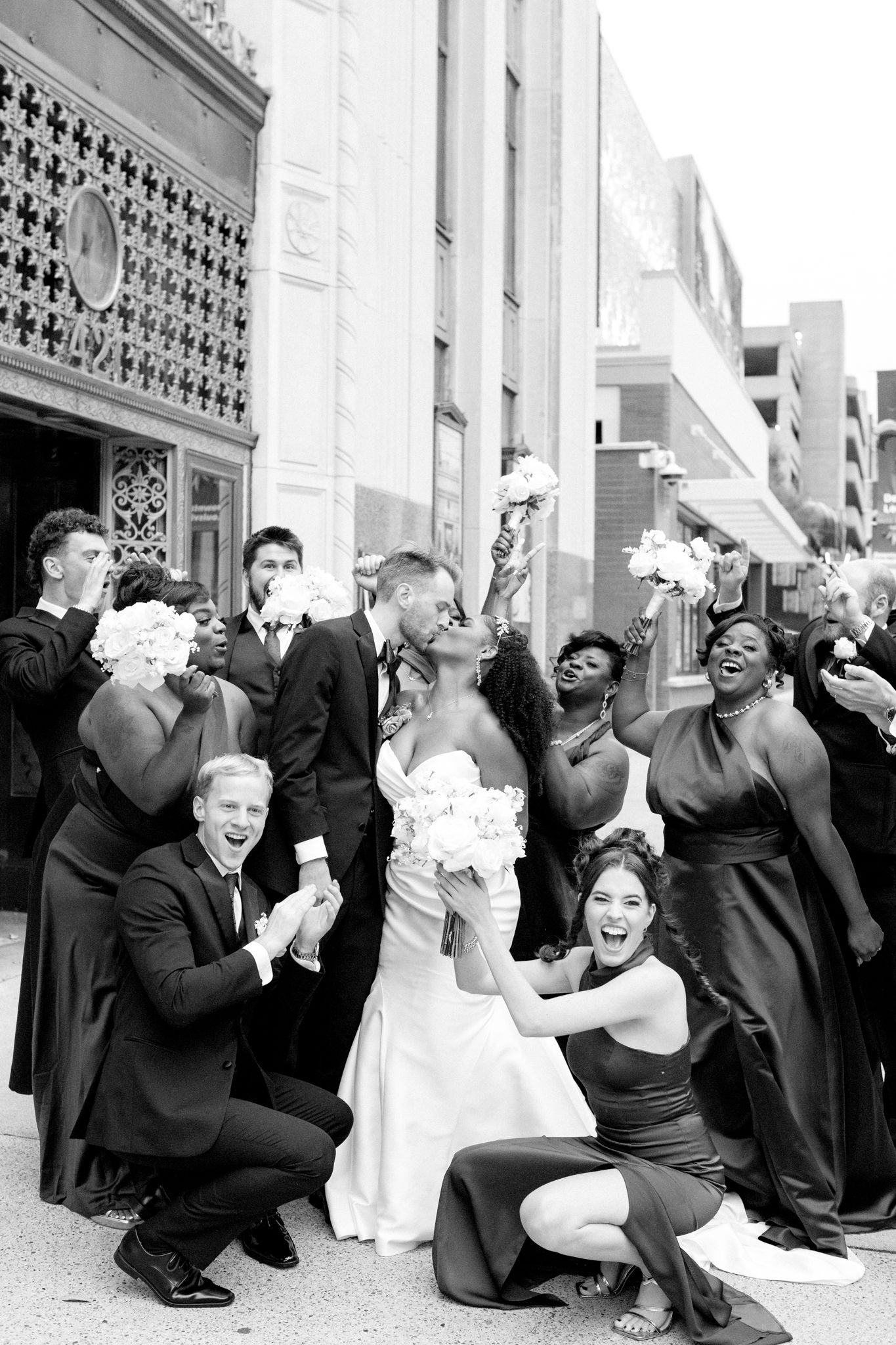 Wedding party members in black attire strike playful poses in a series of candid black and white photos.
