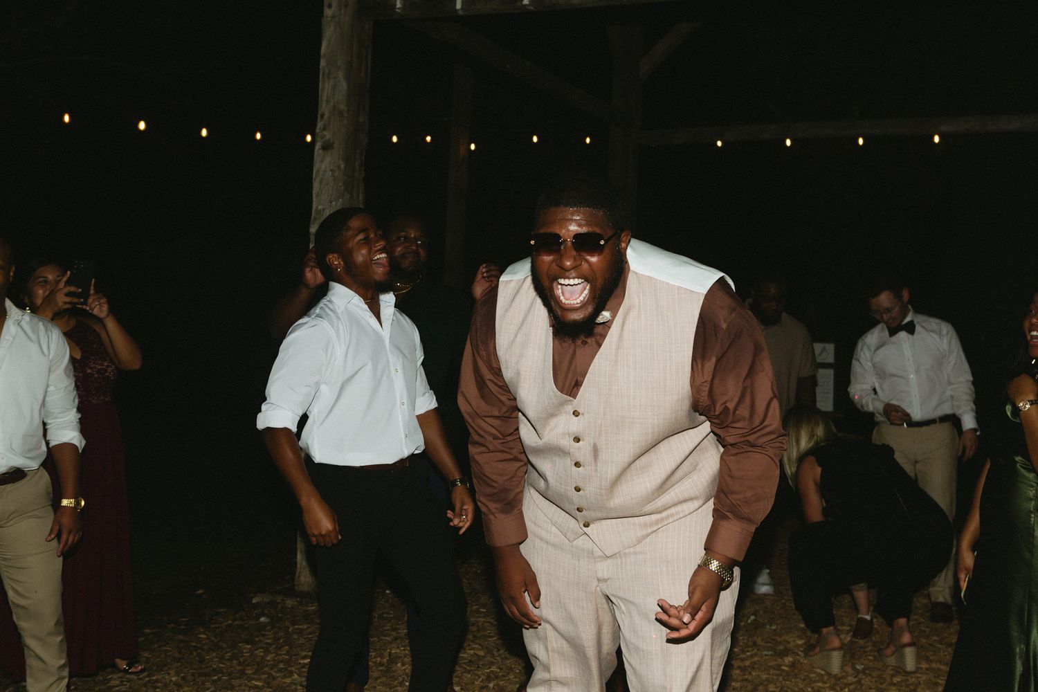A group of people dancing and celebrating at night under string lights at an outdoor party.