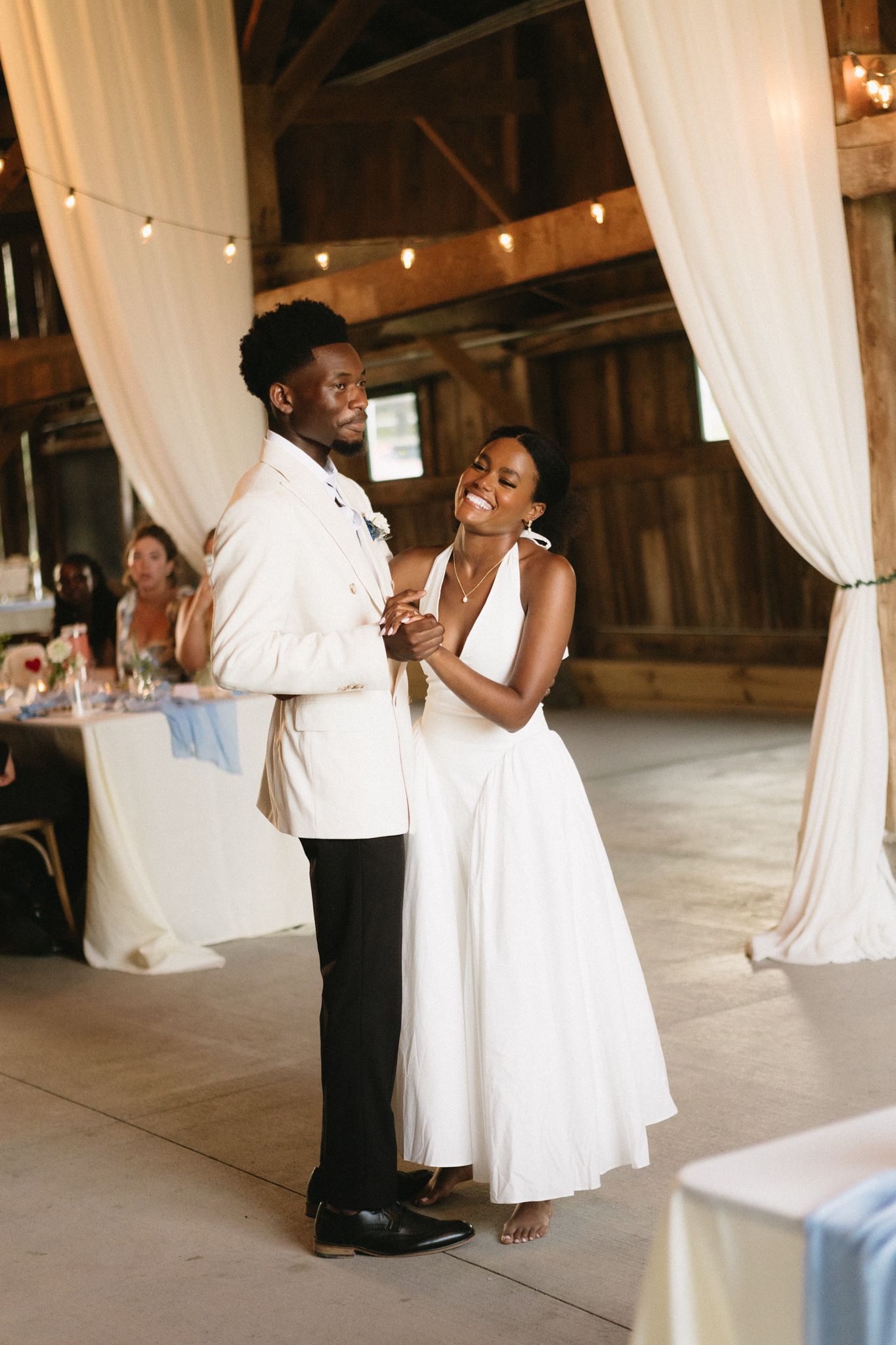 Joyful dance moments between guests at a rustic barn wedding reception with white draping and string lights.