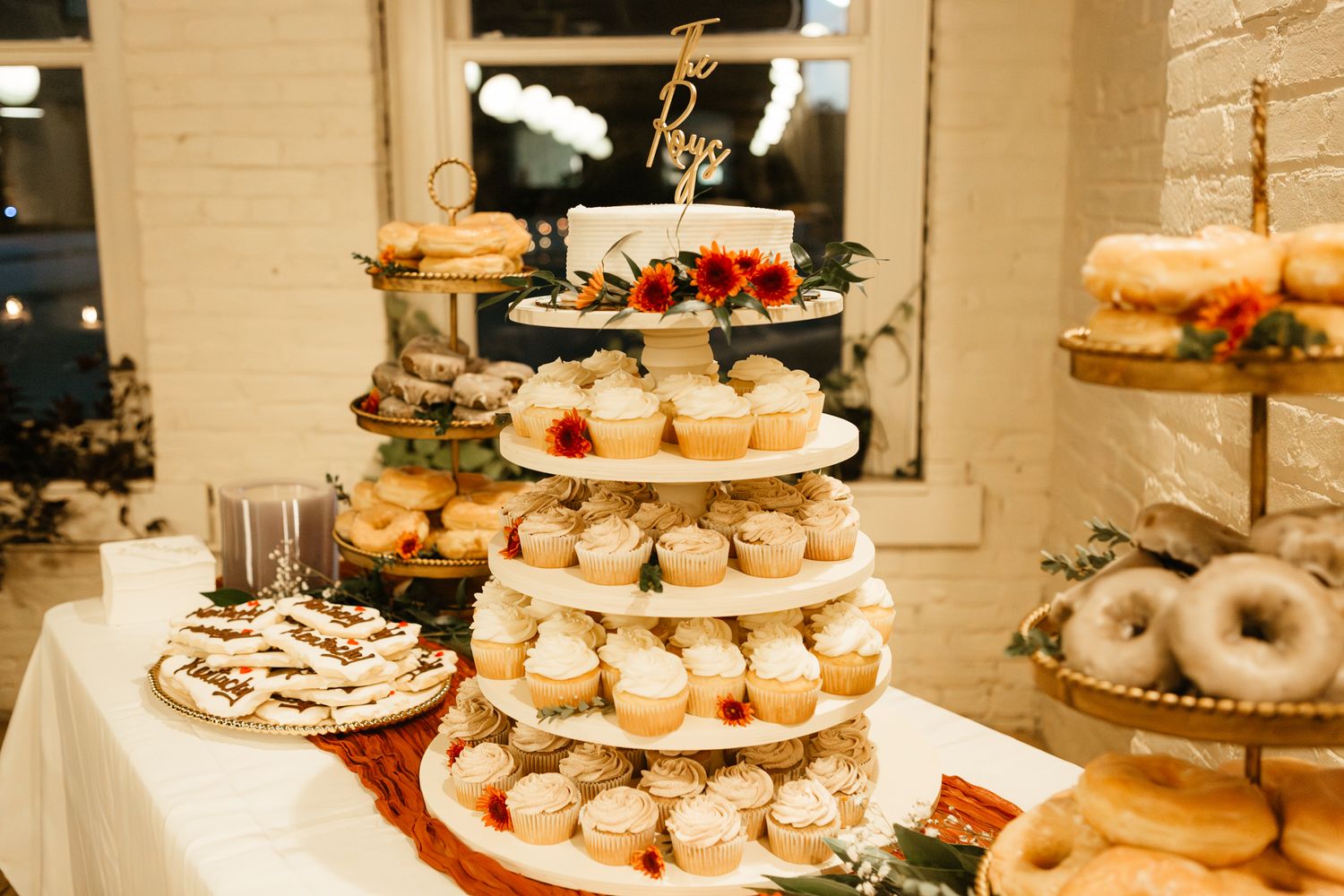 Multi-tiered wedding dessert display with cupcakes, donuts and treats arranged on elegant stands at a reception.
