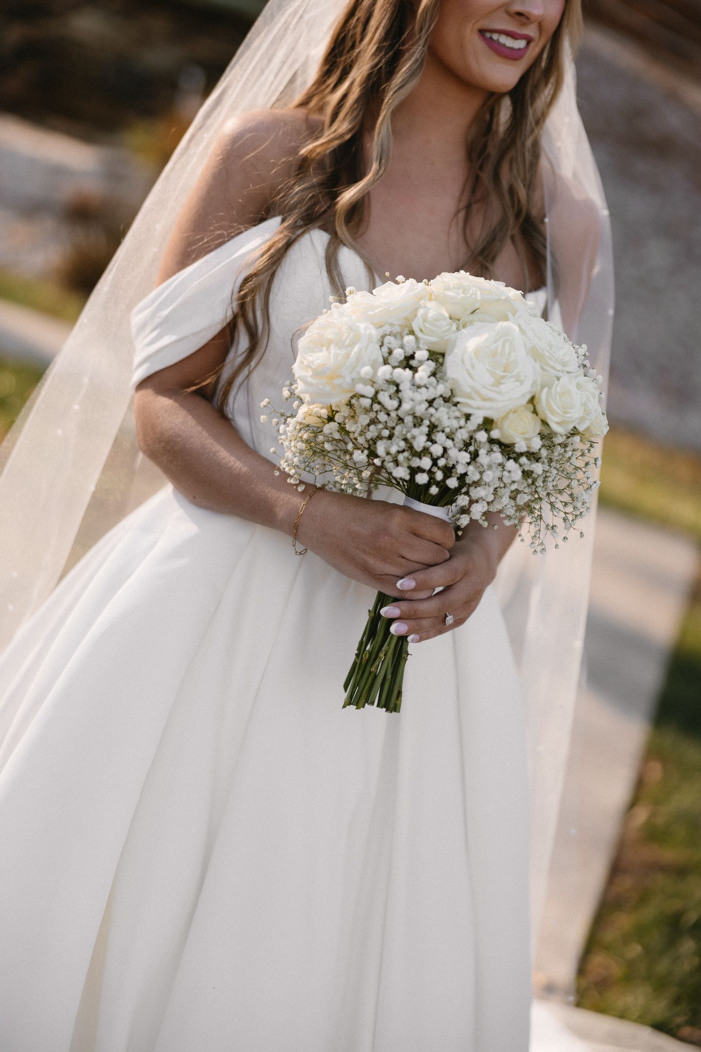 Elegant white bridal bouquet of roses and baby's breath held against a flowing white wedding dress.