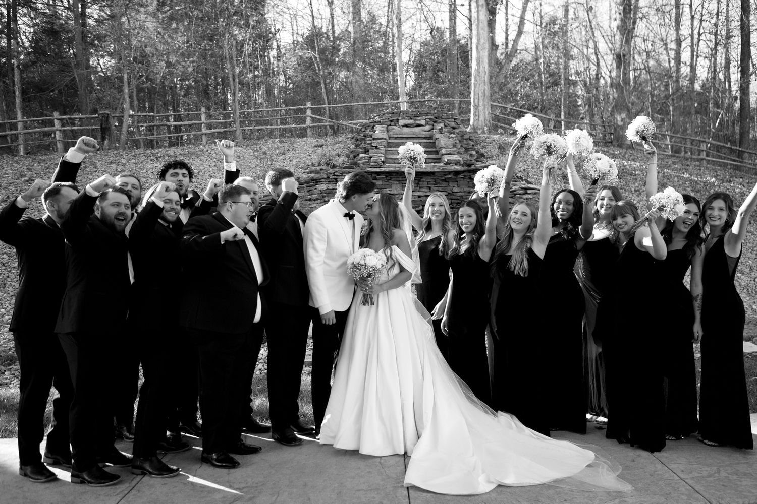Wedding party and guests gather for a celebratory outdoor group photo.