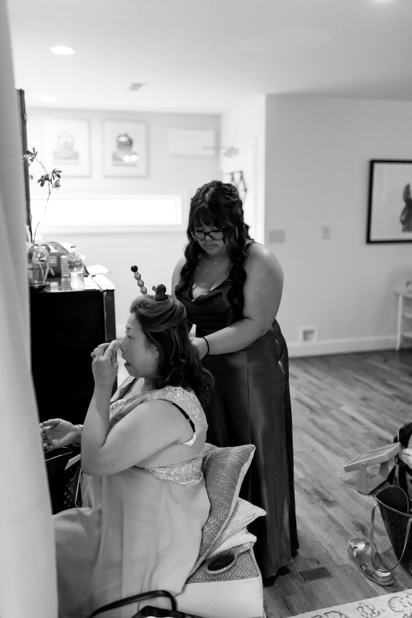 Black and white image of pre-wedding preparations showing someone styling hair in a brightly lit room.