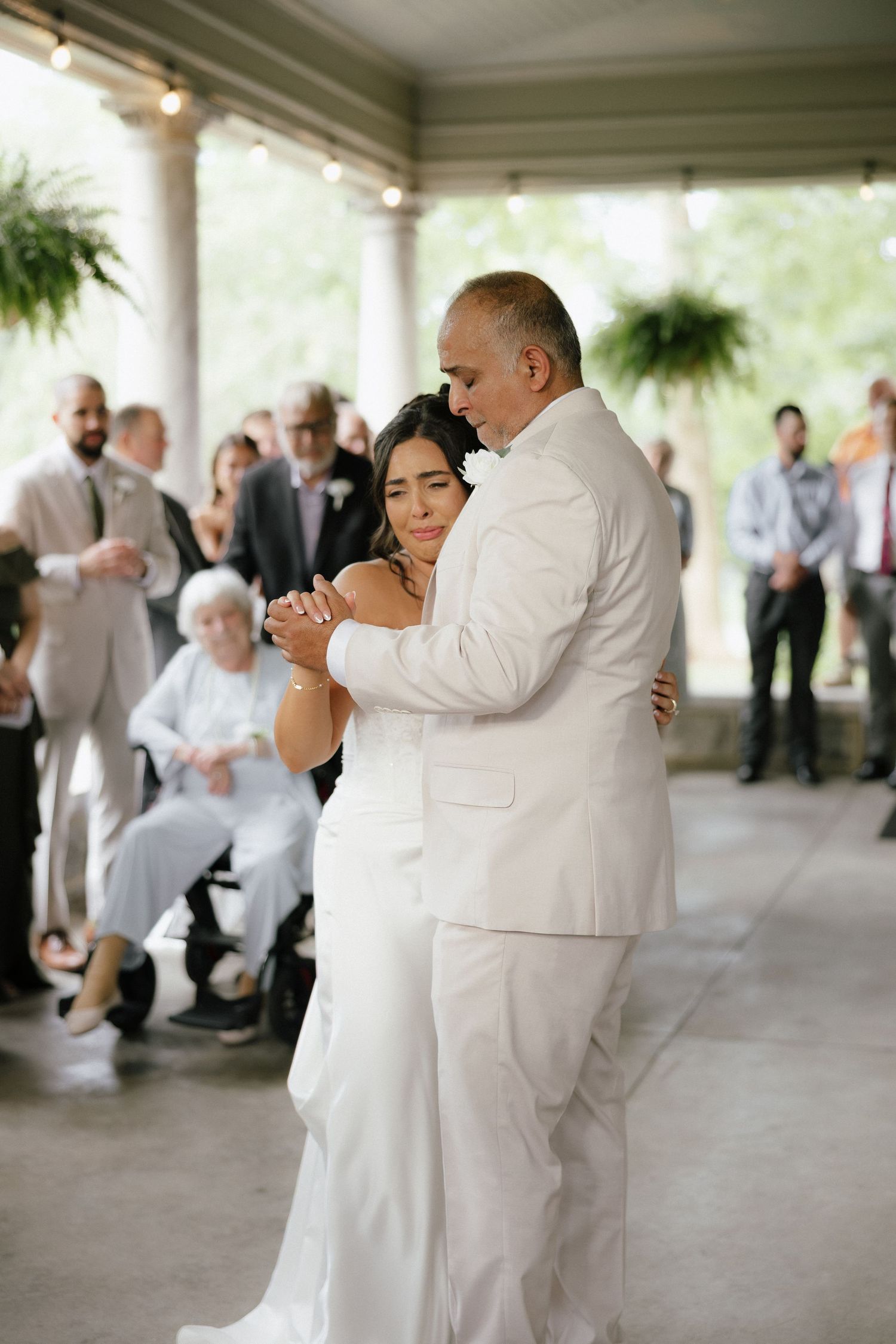 Emotional bride and groom sharing a first dance on a covered porch surrounded by wedding guests.