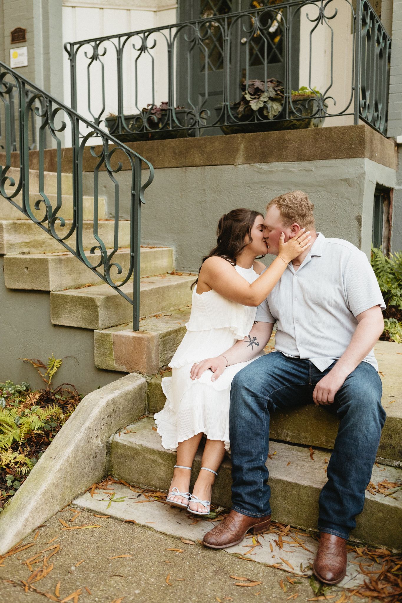 A romantic scene unfolds on urban brownstone steps with vintage iron railings during an engagement shoot.