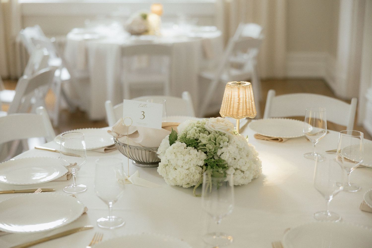 Elegant white wedding reception table with hydrangea centerpiece, gold accents, and glowing candle.