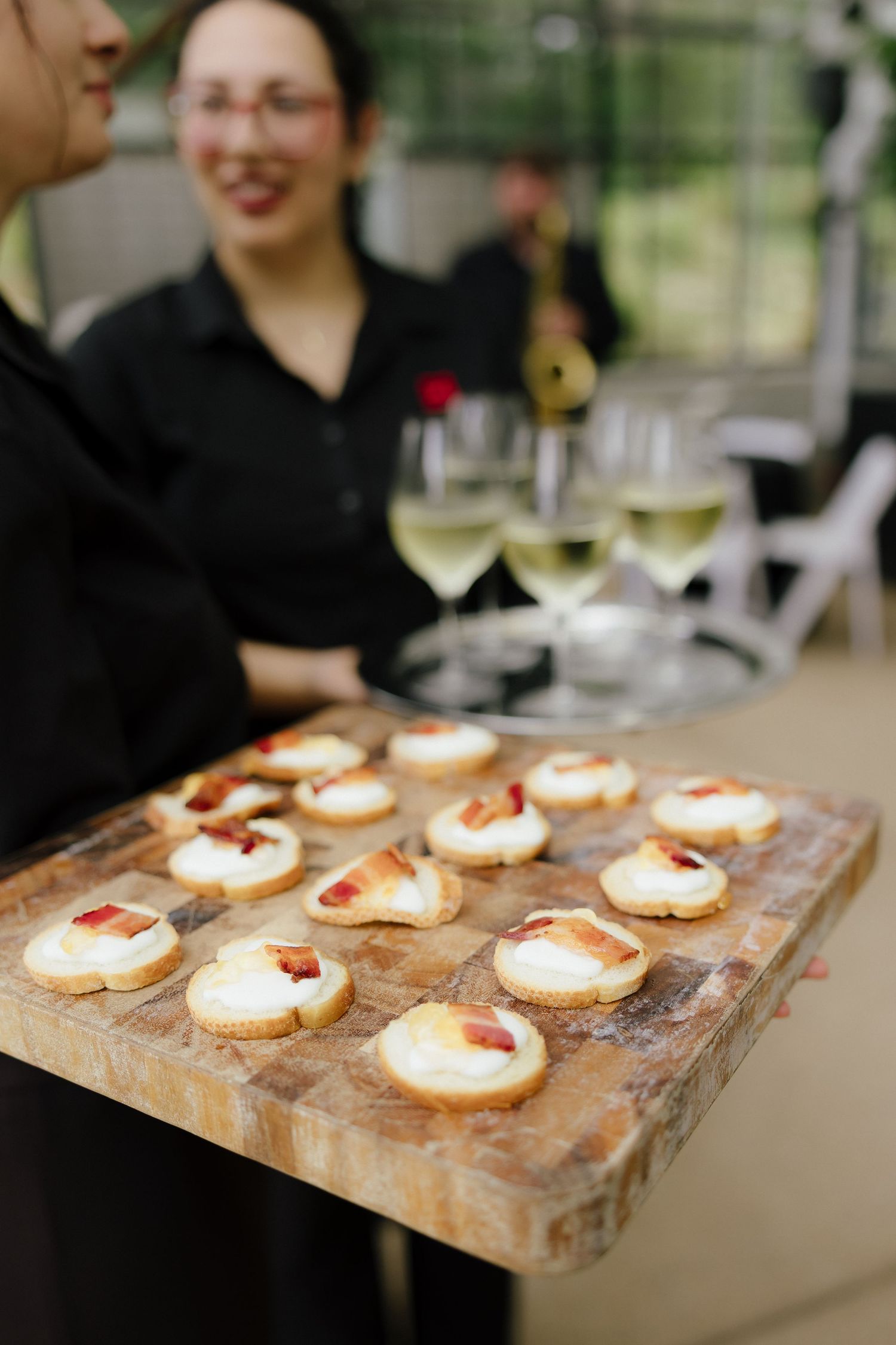 Wedding catering staff serves elegant bruschetta appetizers on wooden board alongside champagne flutes.