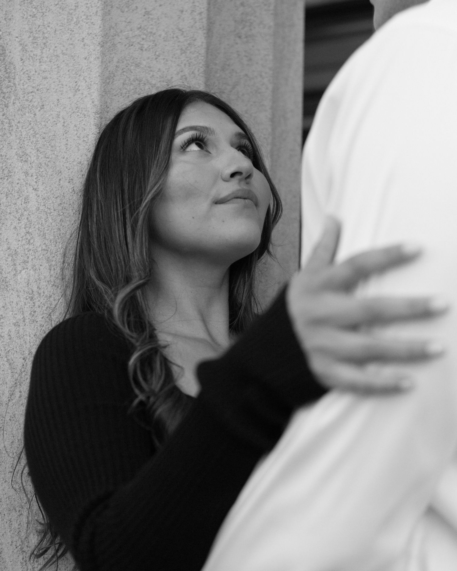 Engaged couple in downtown Louisville, with the woman smiling and showing her engagement ring while embracing her fiancé
