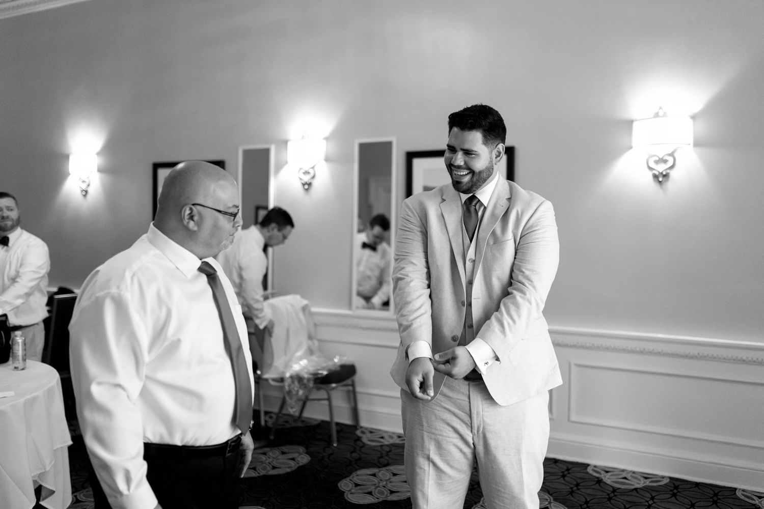 Two people share a candid conversation and laughter in an elegant room with wall sconces and white wainscoting.