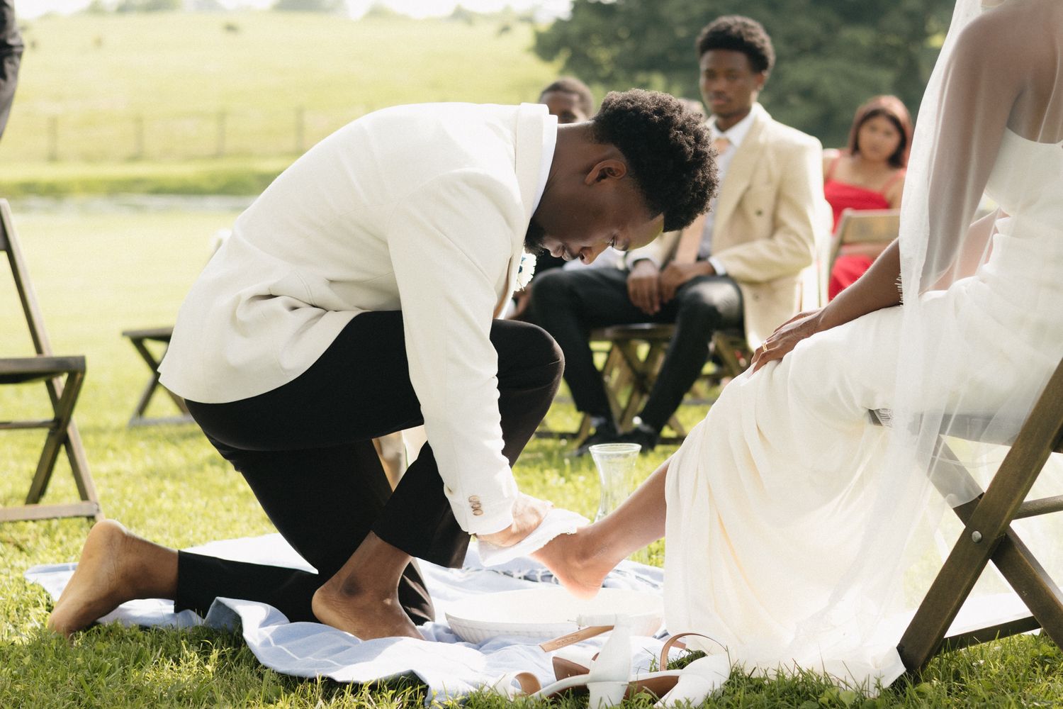 Wedding party members gather outdoors dressed in white attire during daytime celebration.