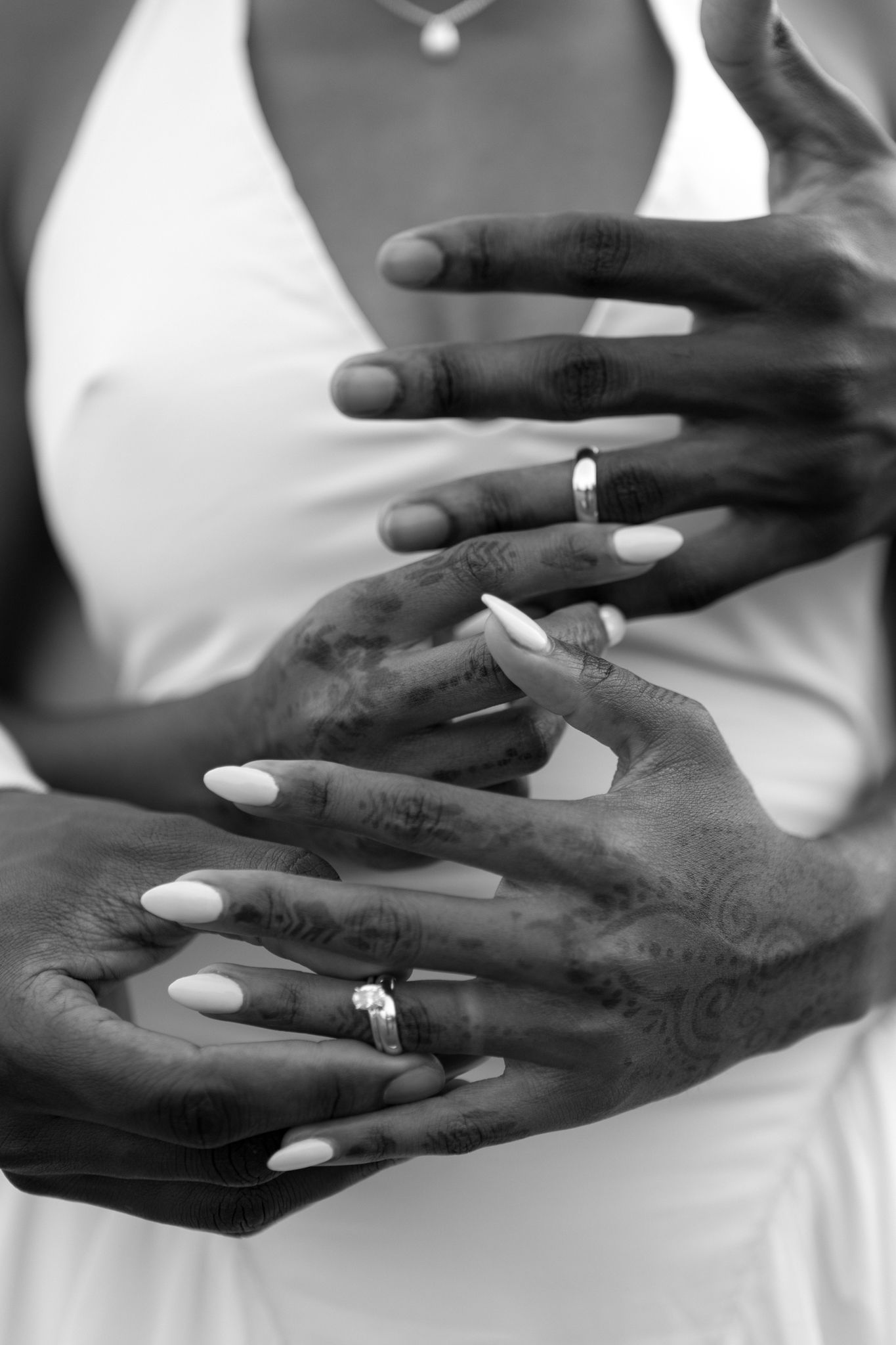 Black and white close-up of hands with wedding rings and white manicured nails.