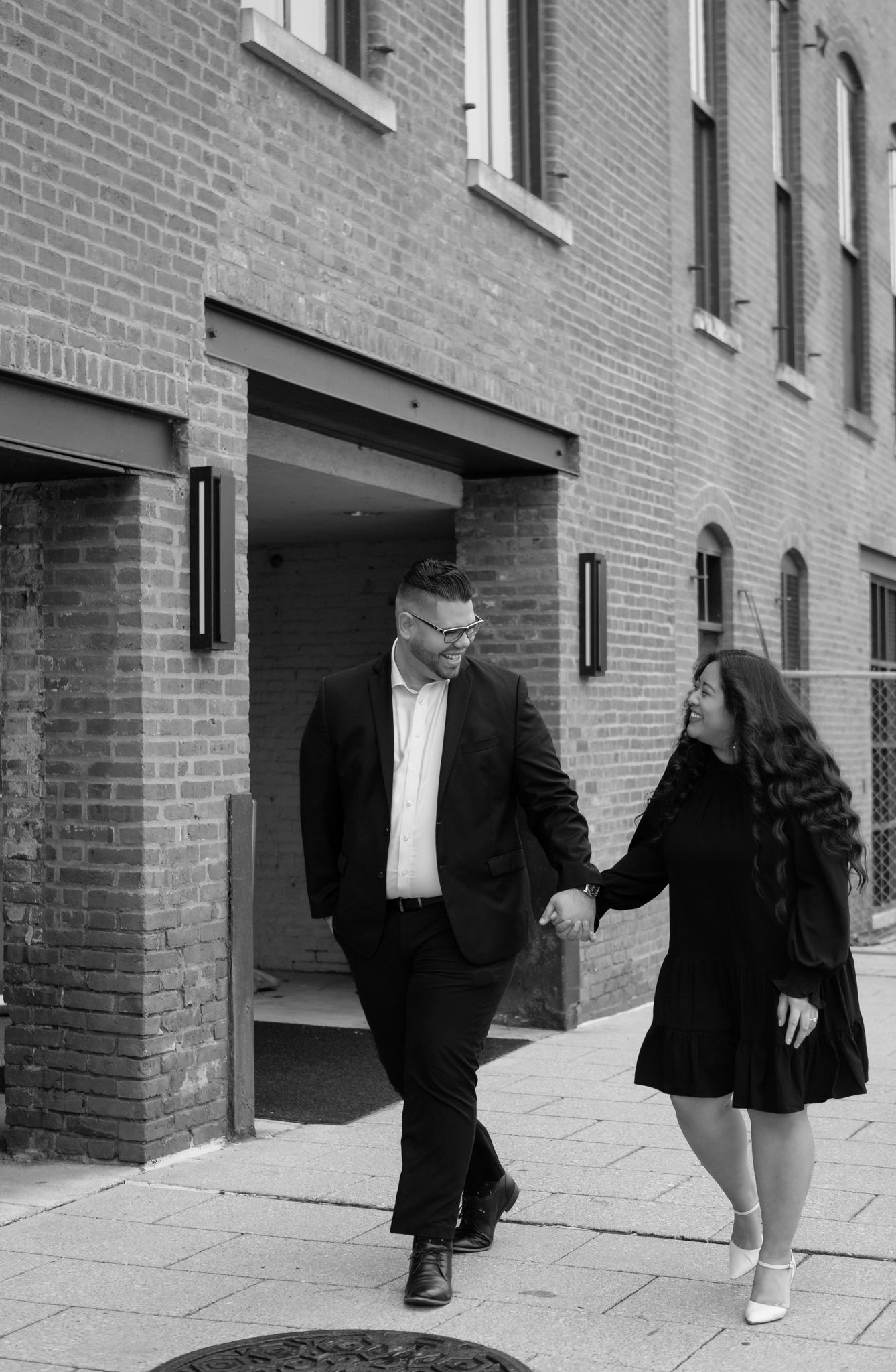 Elegant engaged couple smiling and embracing in downtown Louisville, with the woman showing her engagement ring