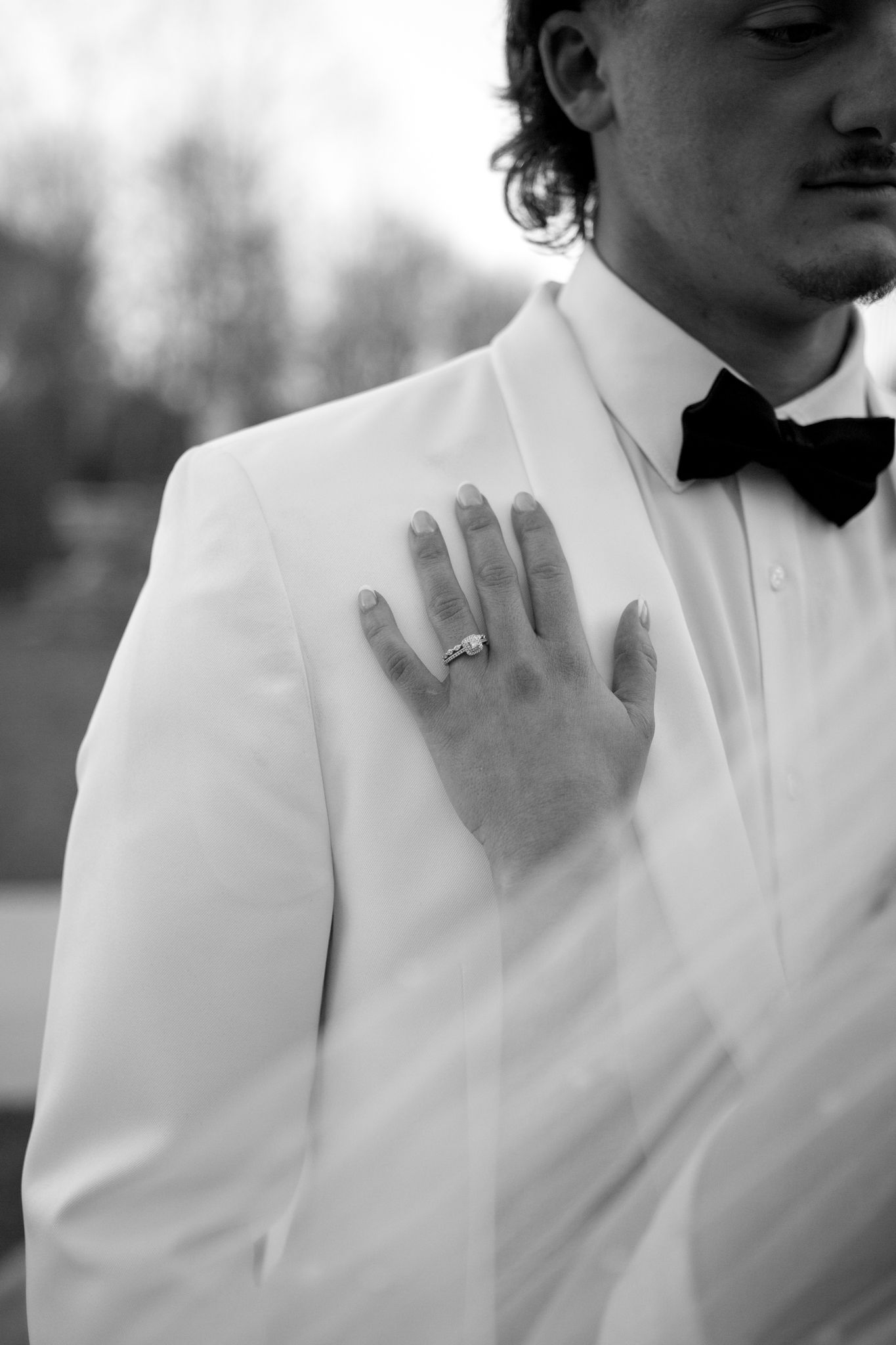 A groom in white adjusts his collar in an artistic black and white photo series.