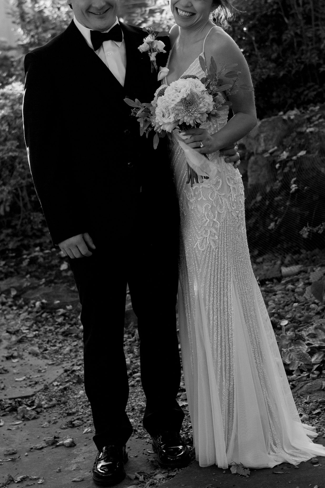 A black and white wedding photo showing a couple dressed in formal attire with a beautiful bouquet.