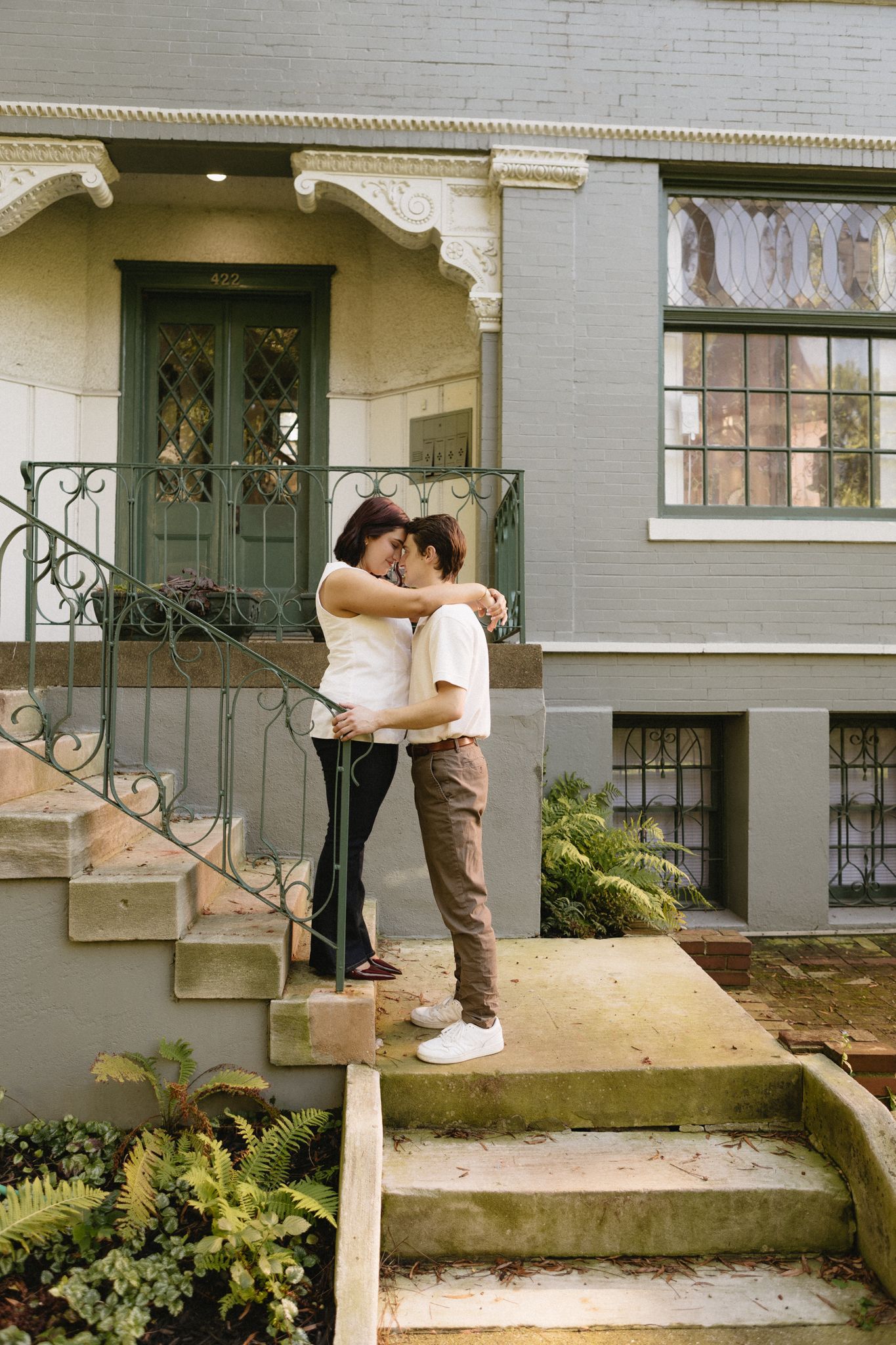 A couple shares a romantic moment on the front steps of a house with green door and railing in a photo series.
