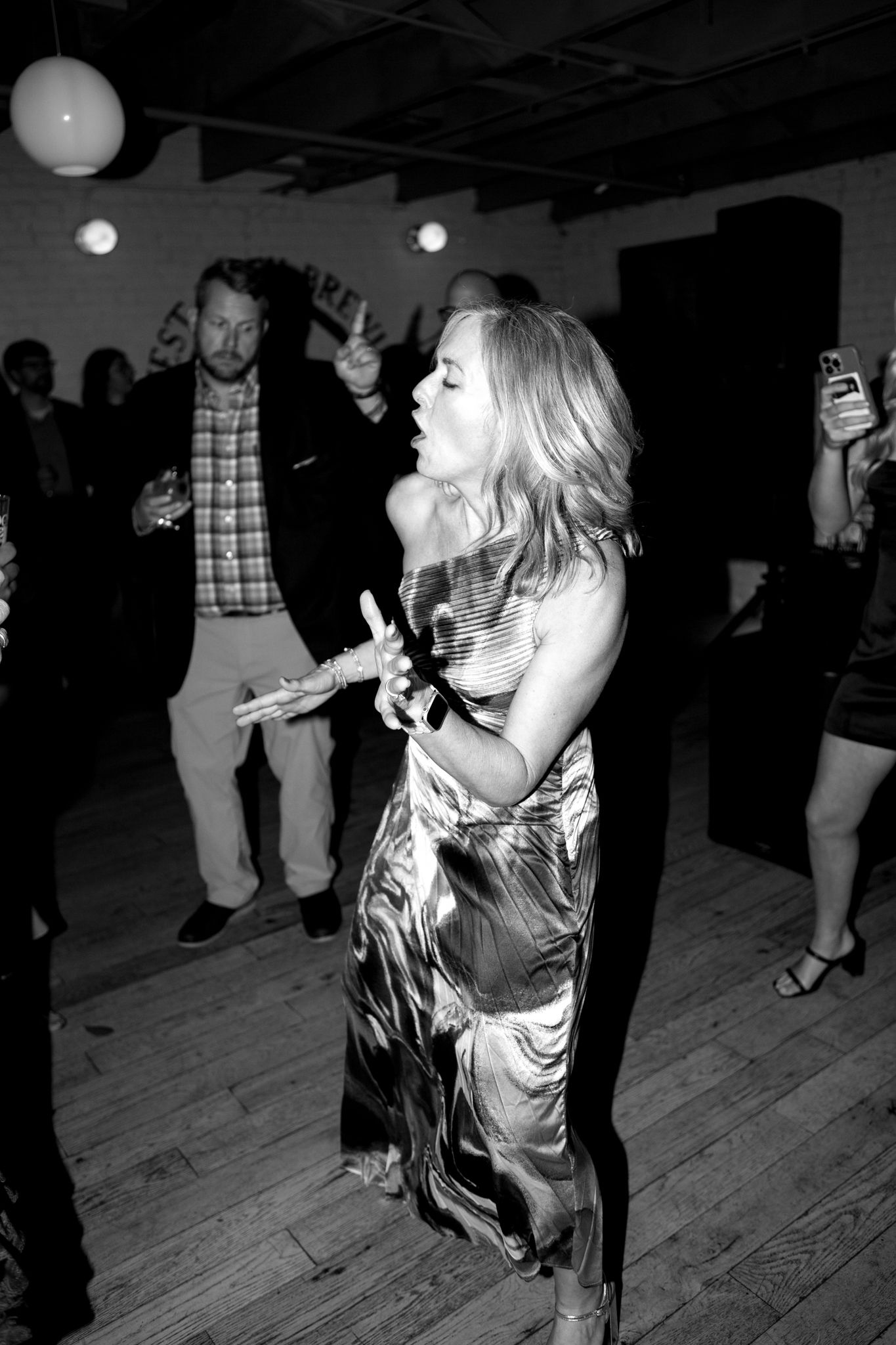 A guest dances energetically at a wedding reception in a flowing patterned dress.